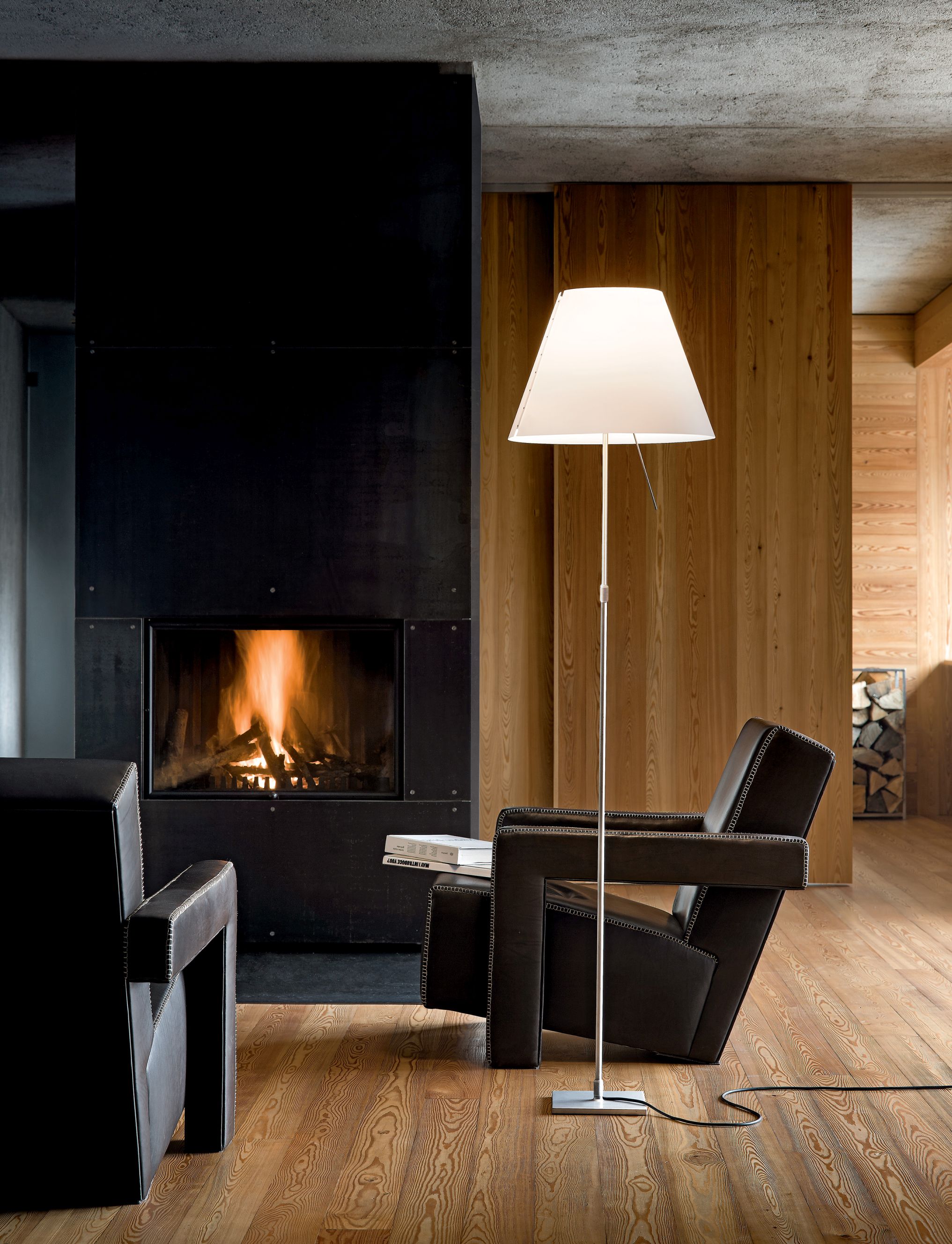 Moderne D13 Costanza Stehleuchte mit Sensordimmer neben Sessel und Kamin für stimmungsvolle Wohnraumbeleuchtung.