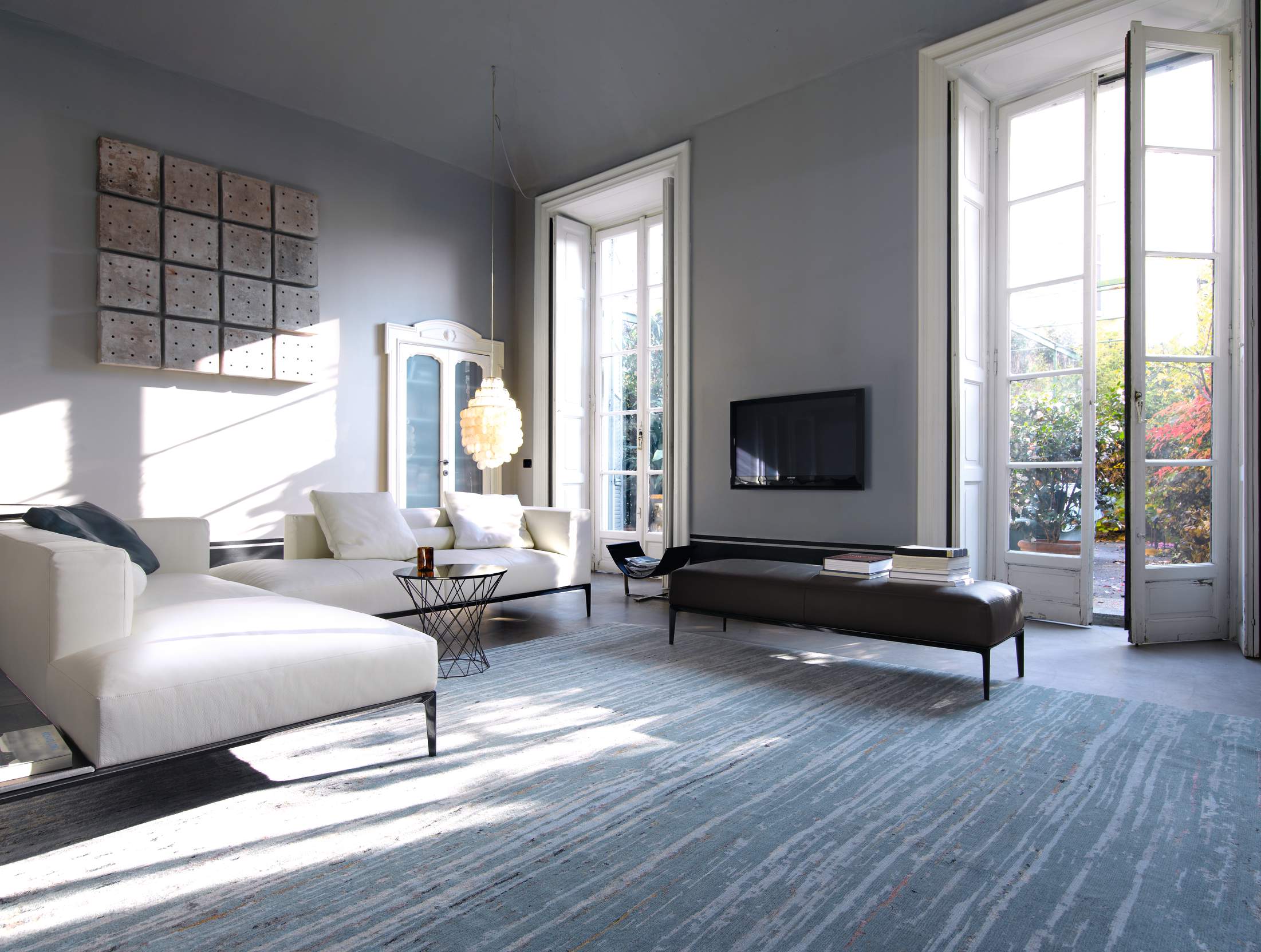 Helles Wohnzimmer mit weißer Ledercouch, Design-Teppich, Fensterfront und moderner Dekoration.