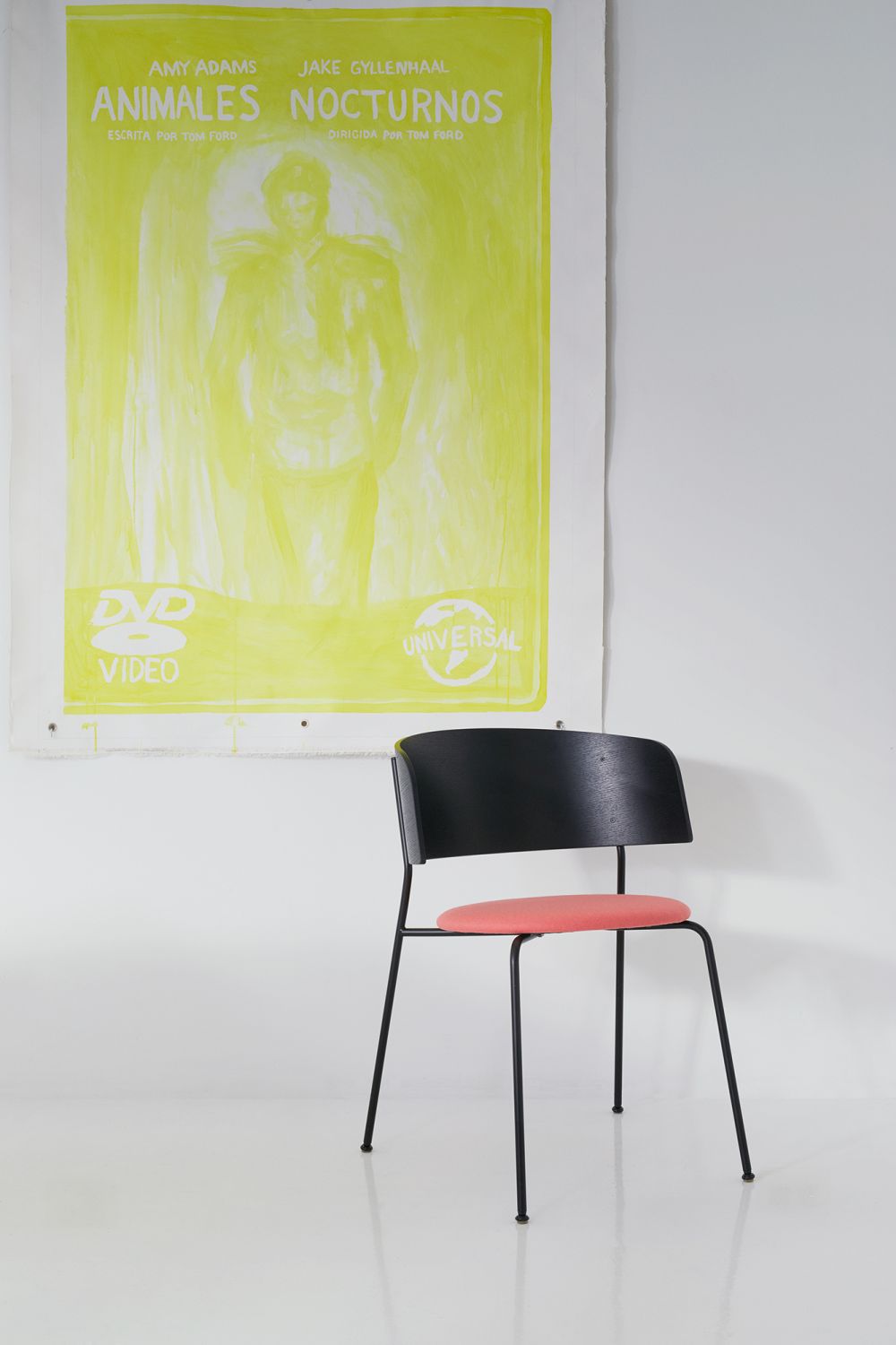 WAGNER Armlehnstuhl mit schwarzem Gestell und roter Sitzfläche vor einem Filmposter.