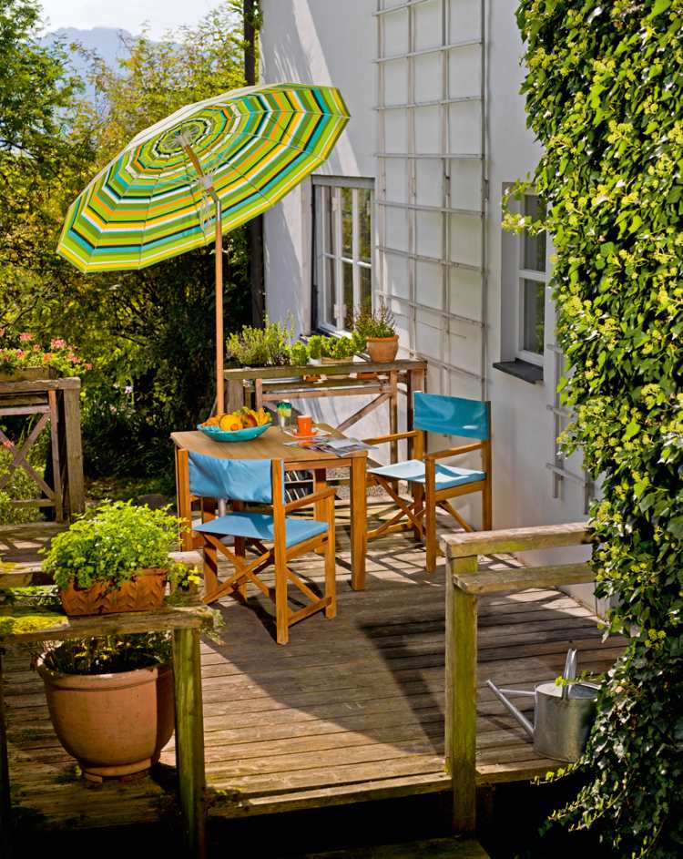 Cabin Sessel von Weishäupl aus Tanne auf einer Holzterrasse mit Tisch und Sonnenschirm.