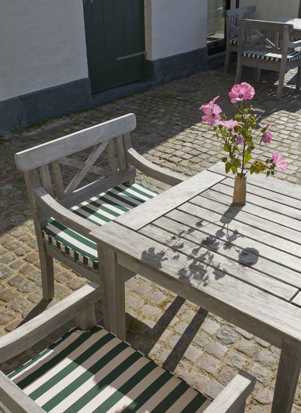 Drachmann Tisch von Skagerak by Fritz Hansen für den Garten mit Stühlen und Blumen.