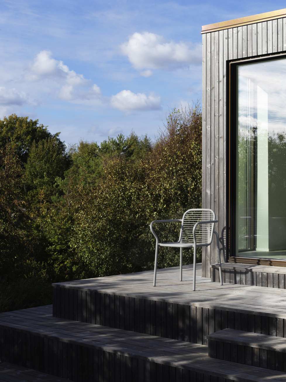 Vig Armchair von Normann Copenhagen: Grauer Outdoor Armlehnstuhl aus Metall auf Holzterrasse vor modernem Haus.