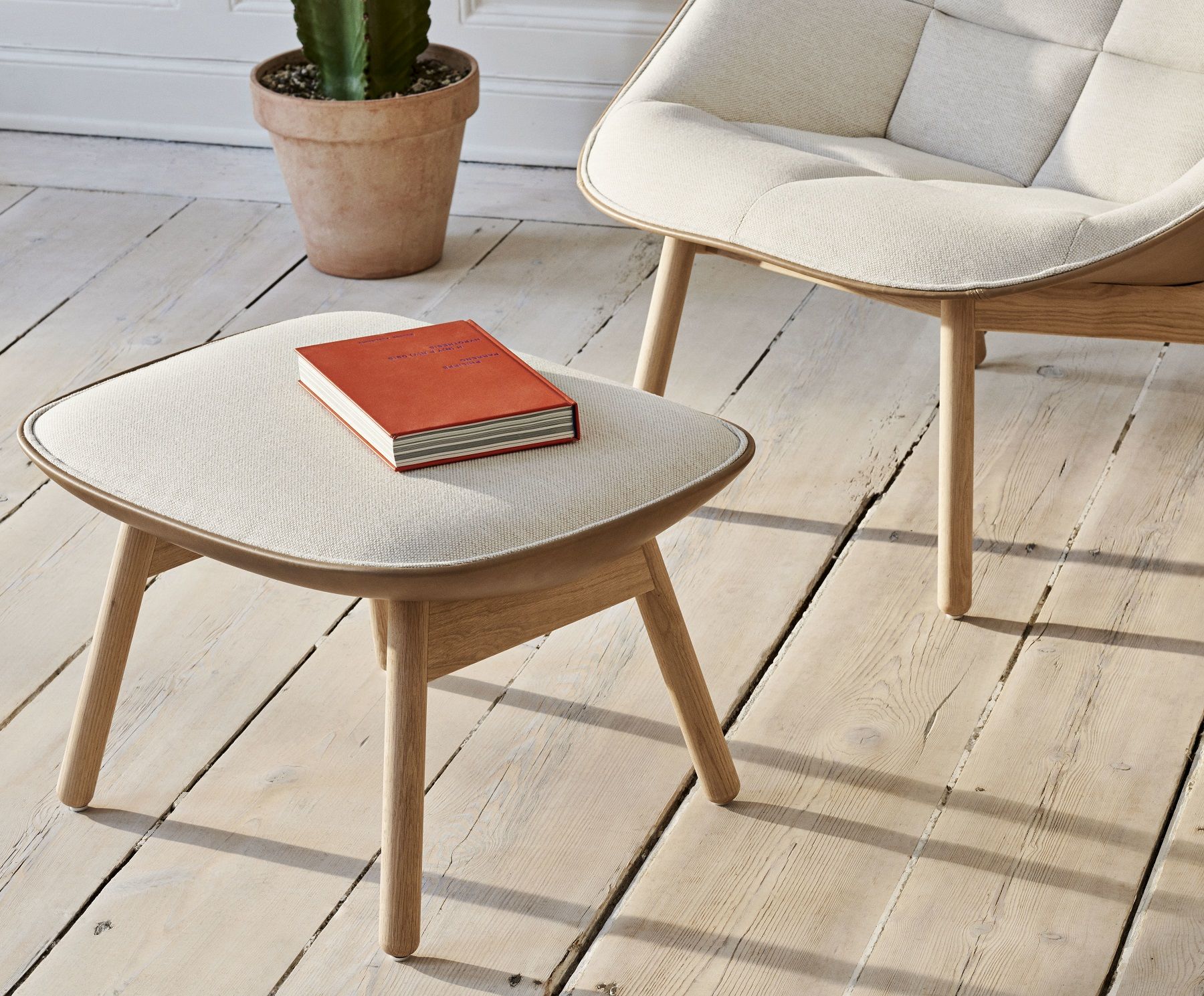 Uchiwa Ottoman Hocker von Hay mit Buch auf hellem Holzboden, Teilansicht des passenden Sessels.
