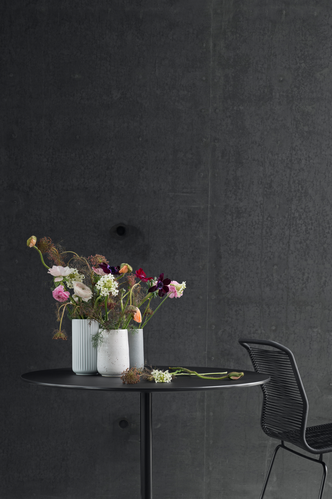 Panton Table Tisch Montana, runder Esstisch in Schwarz mit Blumenvasen und Stuhl vor dunkler Wand.
