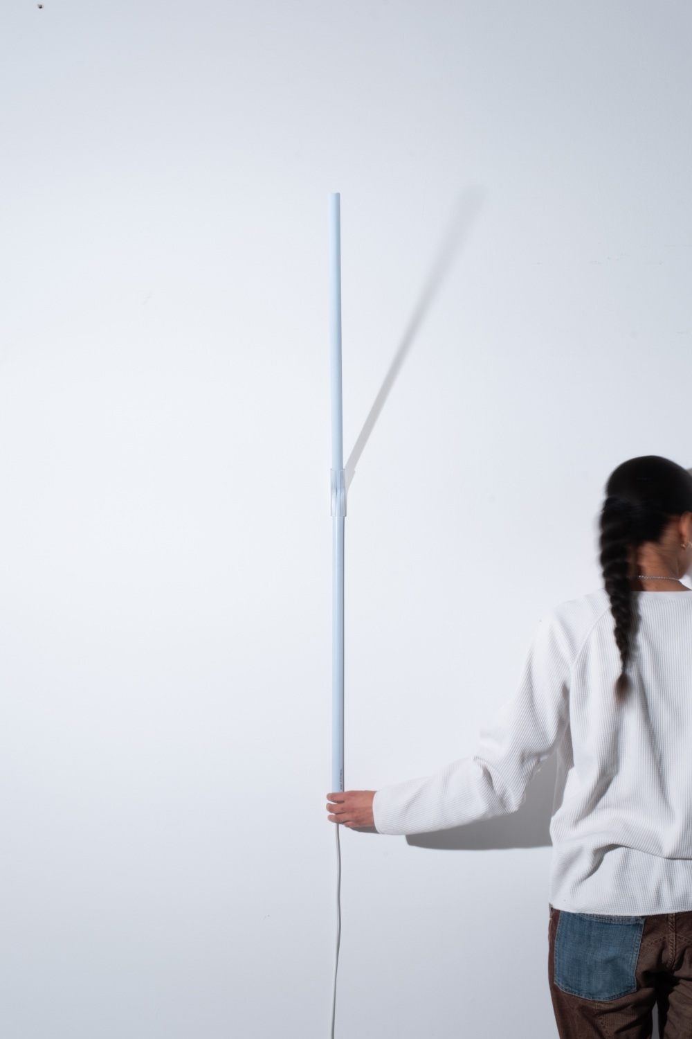 Weiße Measure Light Wandleuchte von Ingo Maurer an einer Wand, gehalten von einer Person.