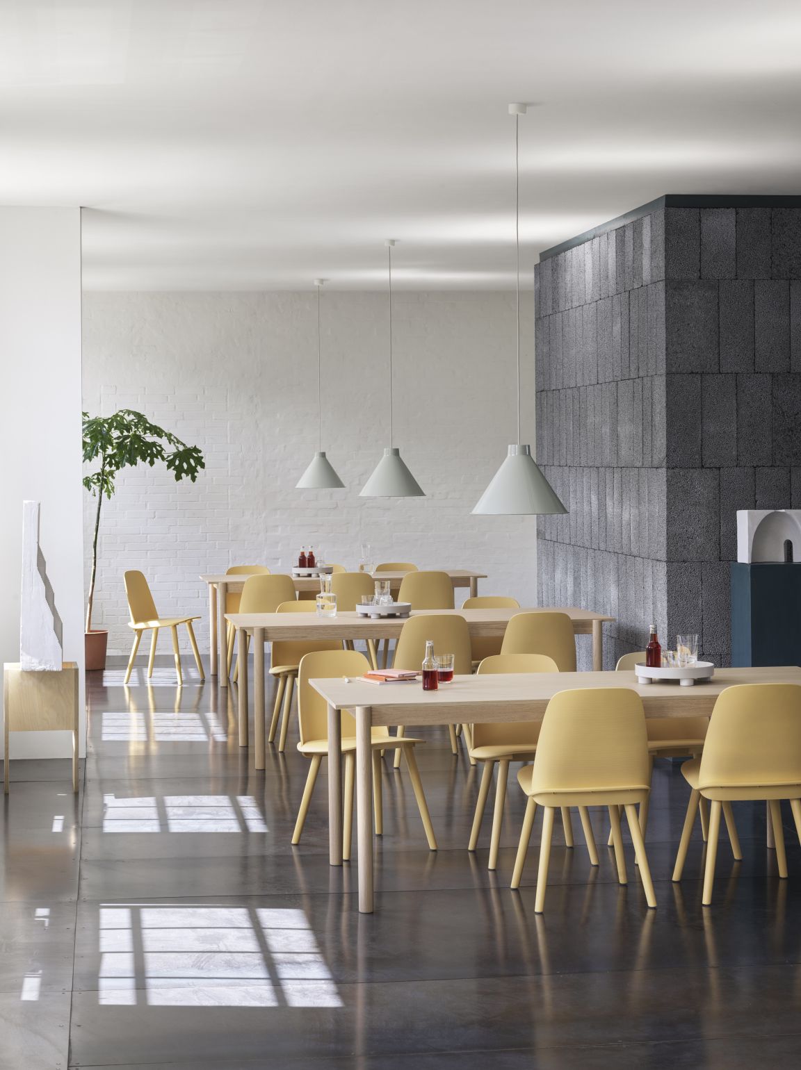 Helles Restaurant mit Tischen, gelben Stühlen und grauen Muuto Top Pendant Pendelleuchten, modernes skandinavisches Design.