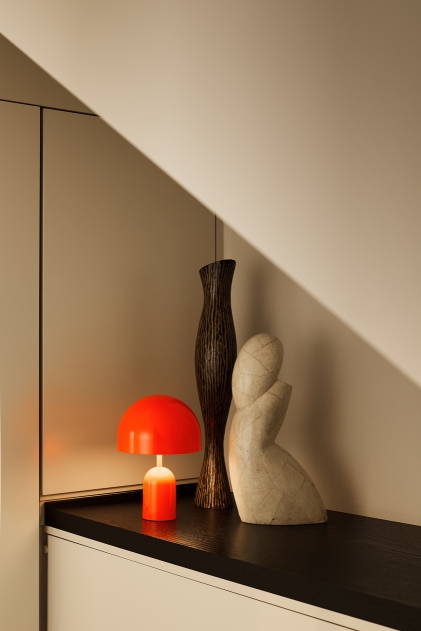 Bell Portable LED Tischleuchte von Tom Dixon in Rot, neben Deko-Objekten auf dunkler Oberfläche.