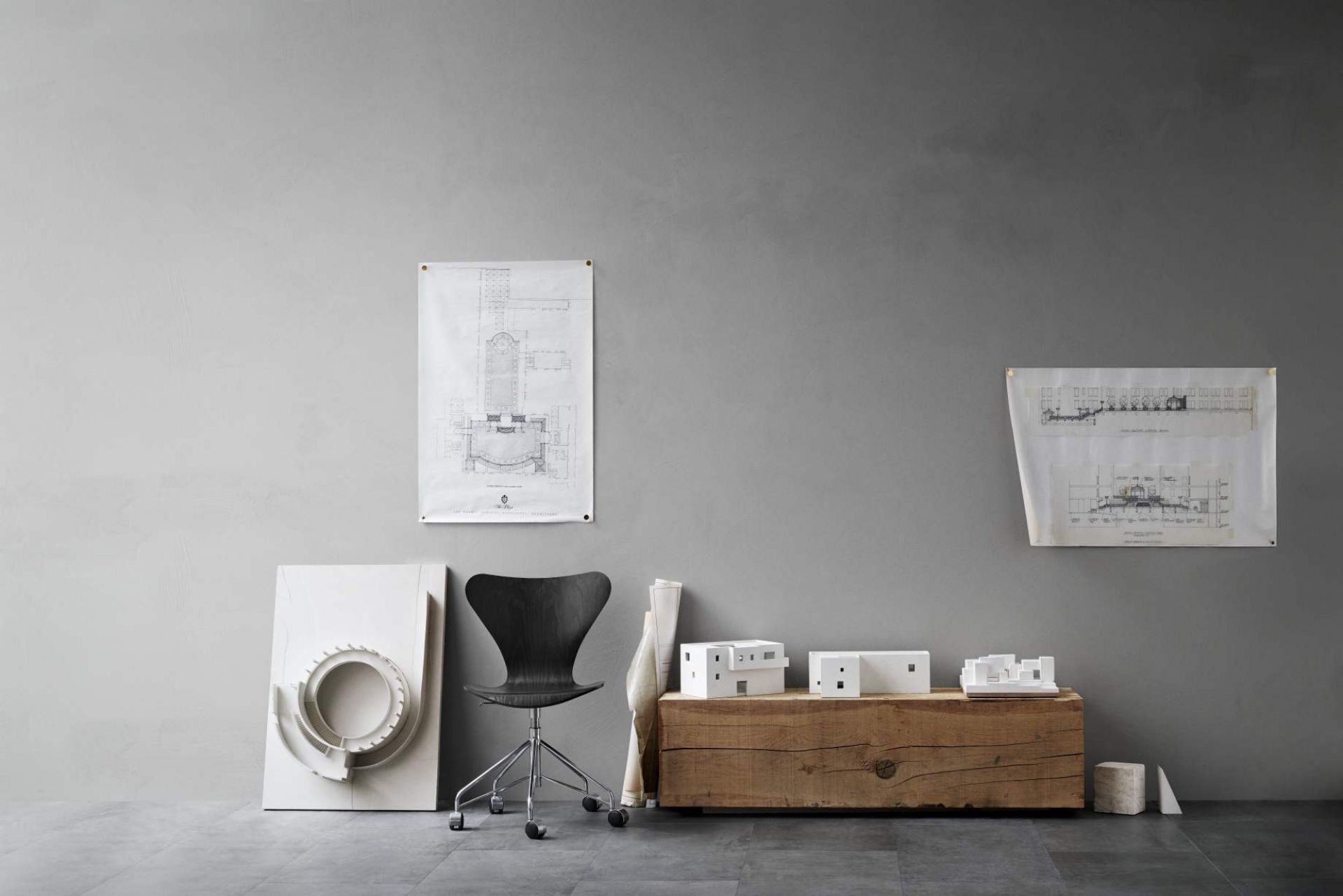 Innenaufnahme mit schwarzem Design Stuhl, Architekturmodellen und Bauplänen an grauer Wand.