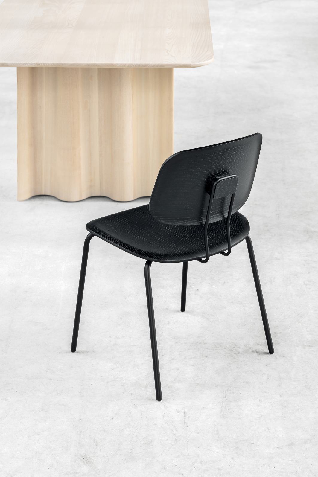 Schwarzer Okito Ply Dining Chair Stuhl Zeitraum mit Holzstruktur und Metallbeinen vor einem Holztisch.