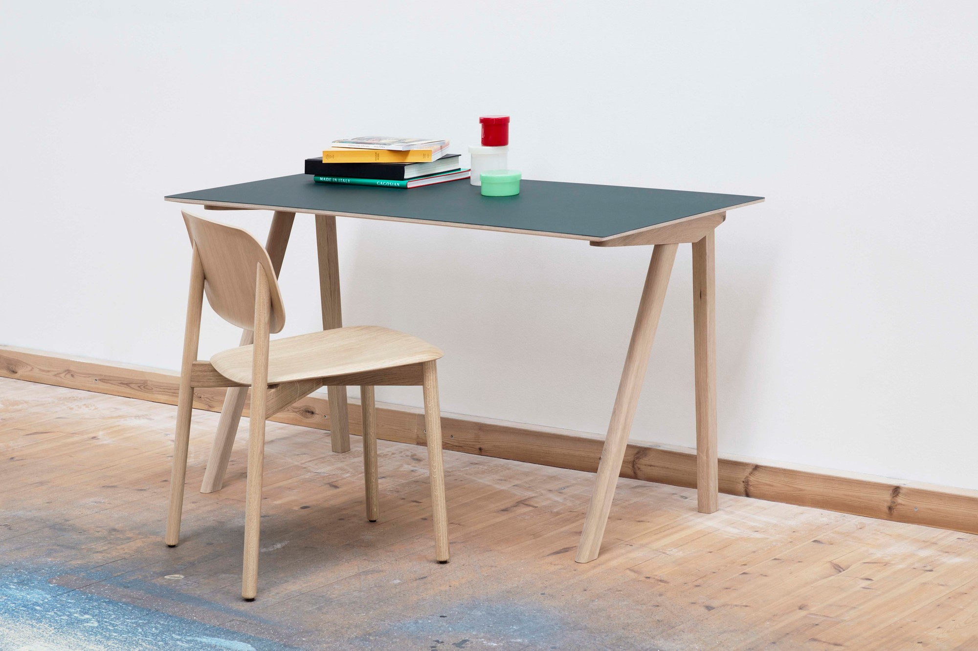 Nahaufnahme eines hellen Holzschreibtisches mit dunkelgrüner Platte und einem Soft Edge Stuhl von Hay im minimalistischen Design.
