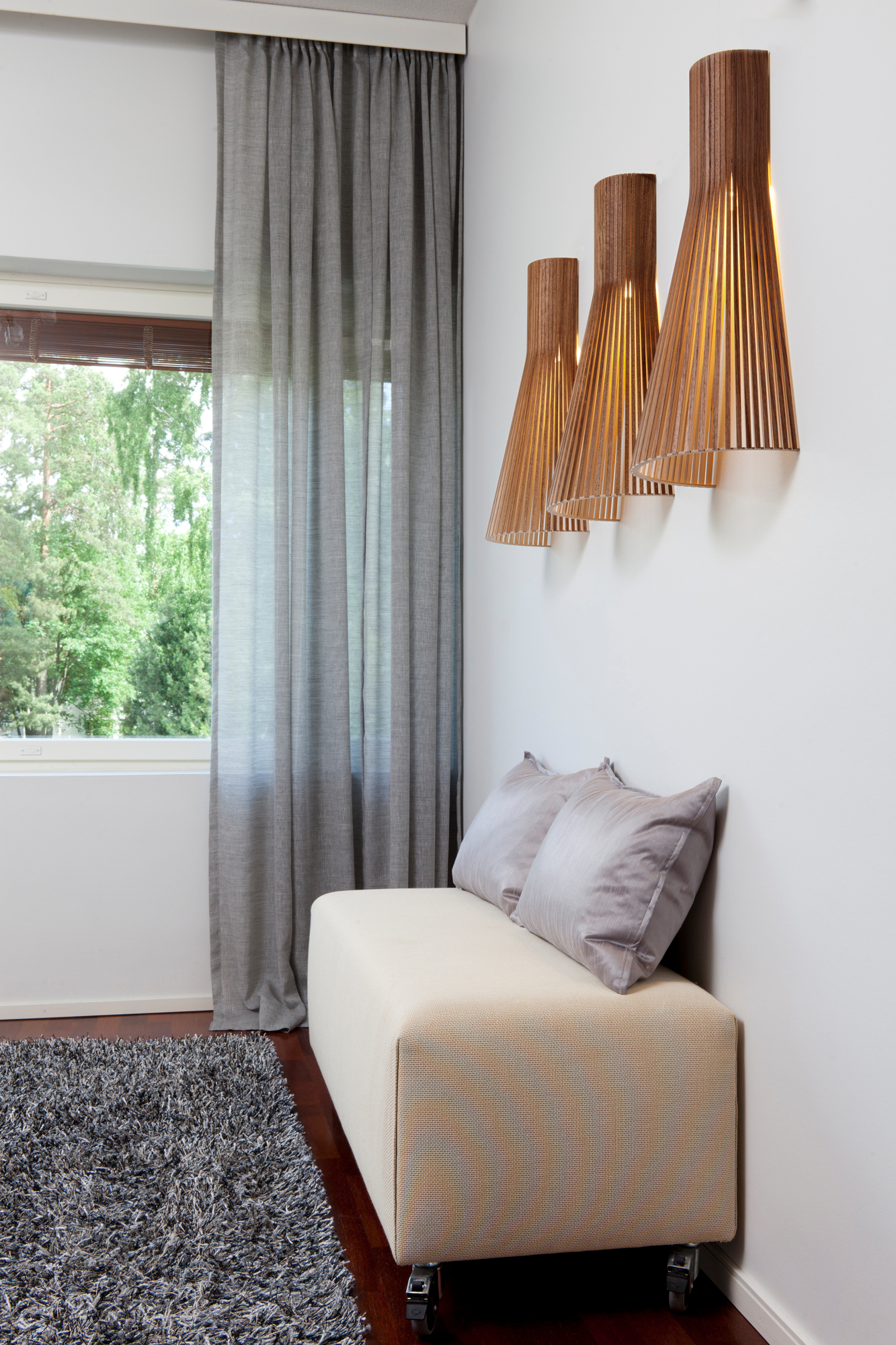 Secto 4230 LED Wandleuchte aus Holz über einer Sitzbank mit Kissen im Wohnzimmer.