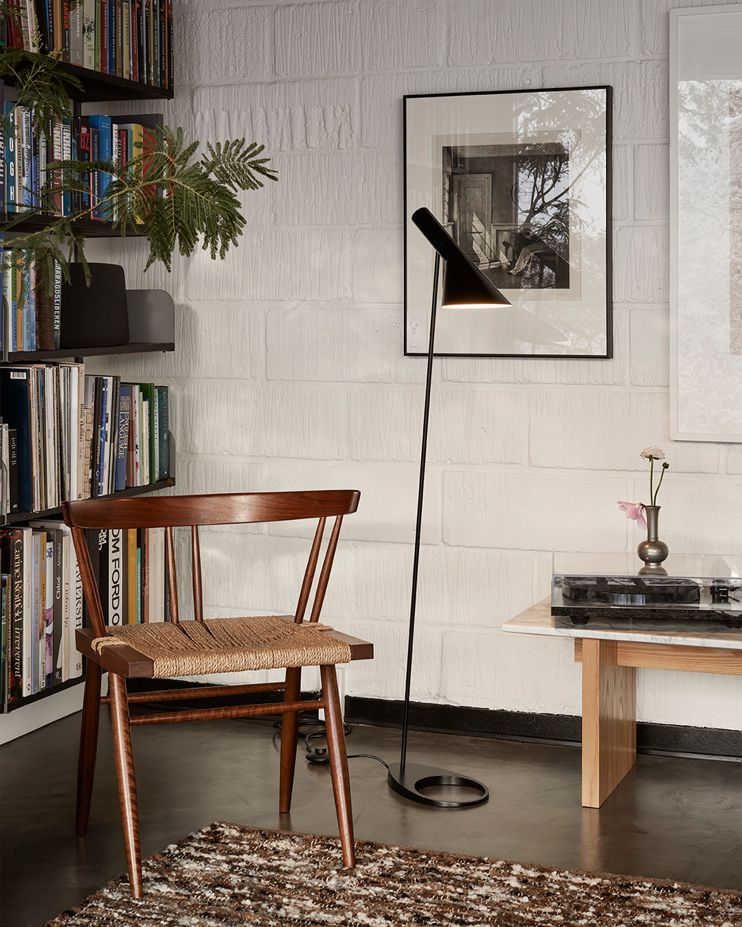 Schwarze Stehlampe im skandinavischen Design neben Holzstuhl mit Seilgeflecht und Beistelltisch im Wohnzimmer.