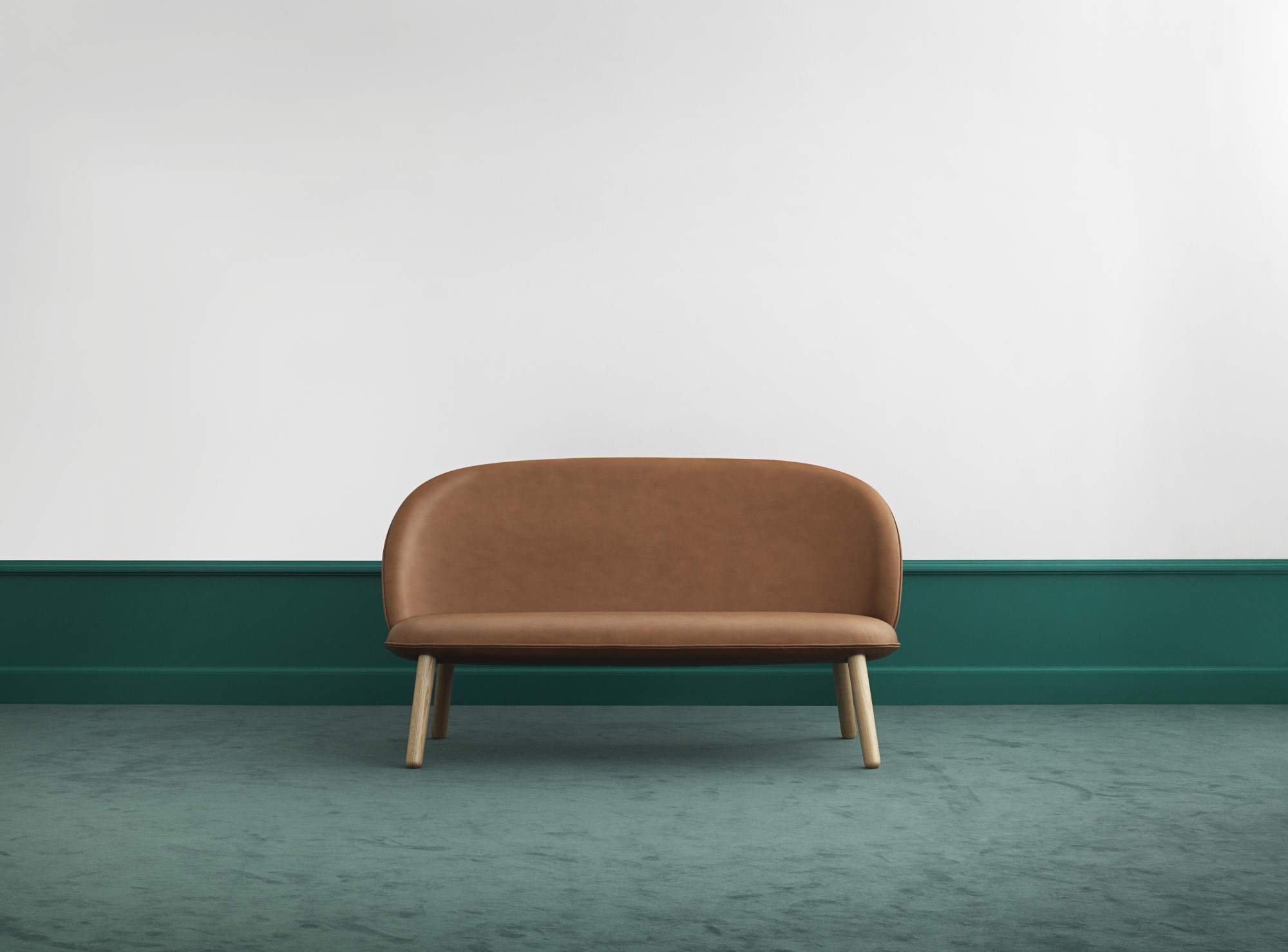 Ace Sofa von Normann Copenhagen in Brandy-Leder mit Holzbeinen vor grüner Wand.