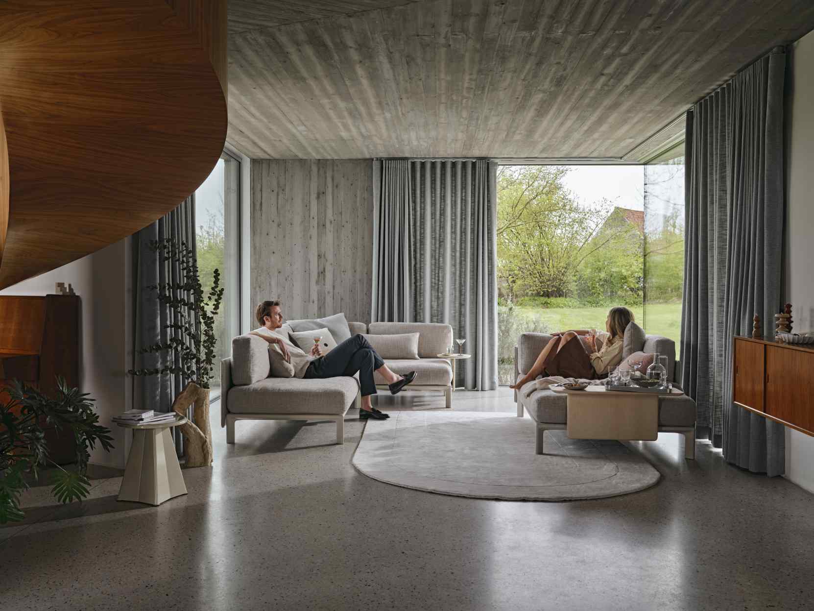 Helle Wohnzimmer-Szene mit zwei Personen auf dem Vitra Anagram Sofa Plattform, modernes Möbeldesign.
