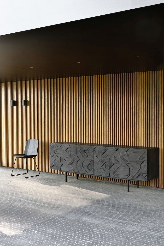 Schwarze Graphic Teak Anrichte von Ethnicraft mit geometrischem Muster und passendem Stuhl vor Holzpaneelwand.