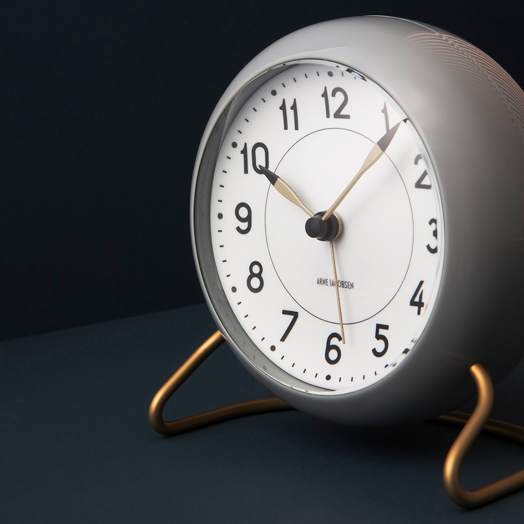 Grau-weisse Arne Jacobsen Station Tischuhr von Rosendahl Timepieces mit goldenem Standfuß. Design-Klassiker für Nachttisch und Büro.
