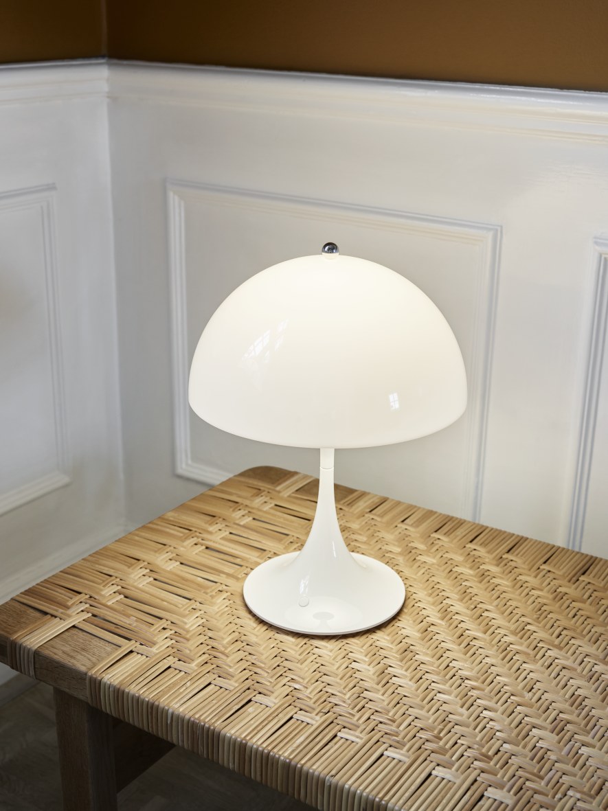 Weiße Panthella 250 Akku LED-Tischleuchte von Louis Poulsen auf einem geflochtenen Tisch.