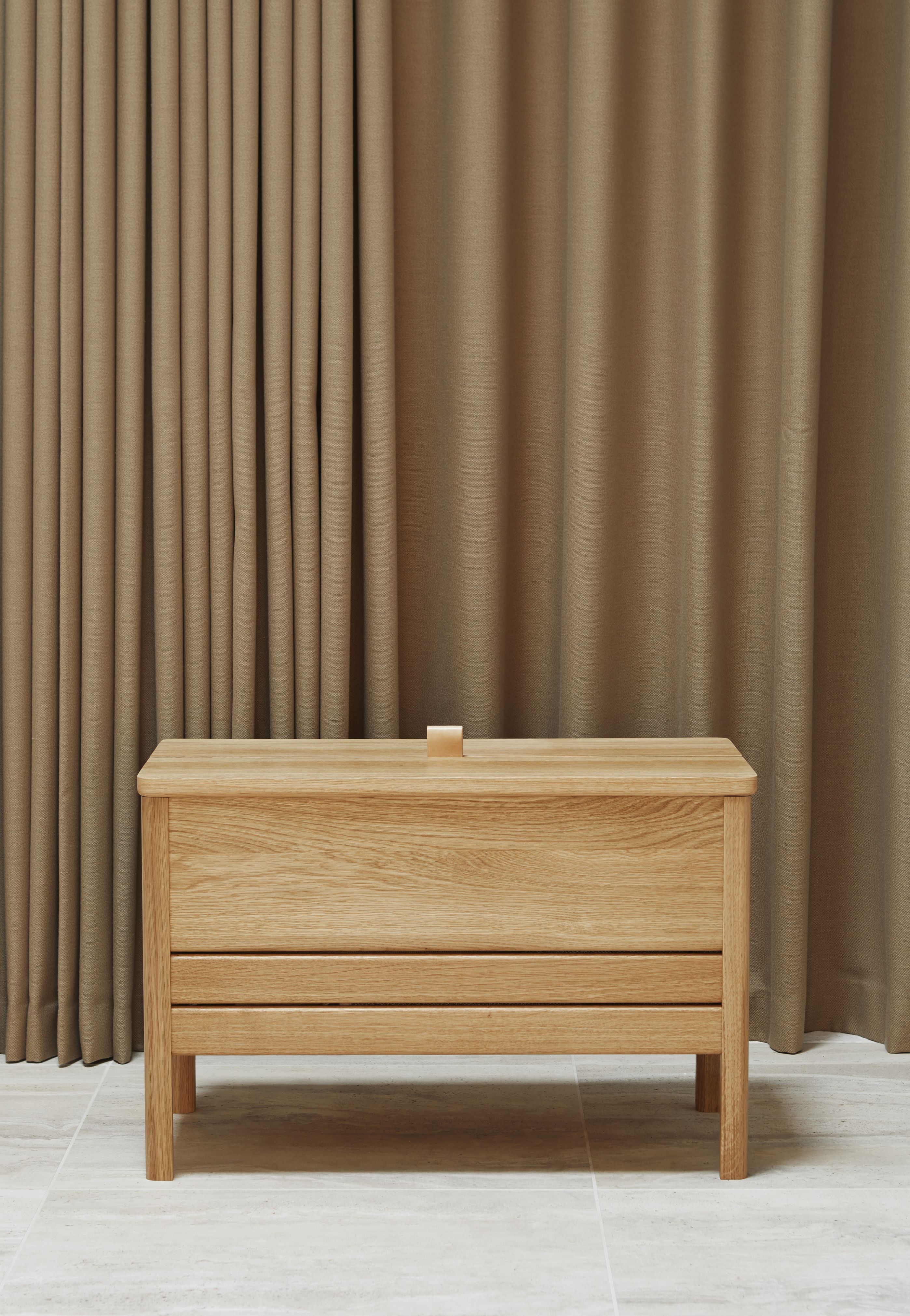 A Line Truhenbank aus Eiche von Form & Refine, helle Holzbank mit Stauraum vor beigem Vorhang.