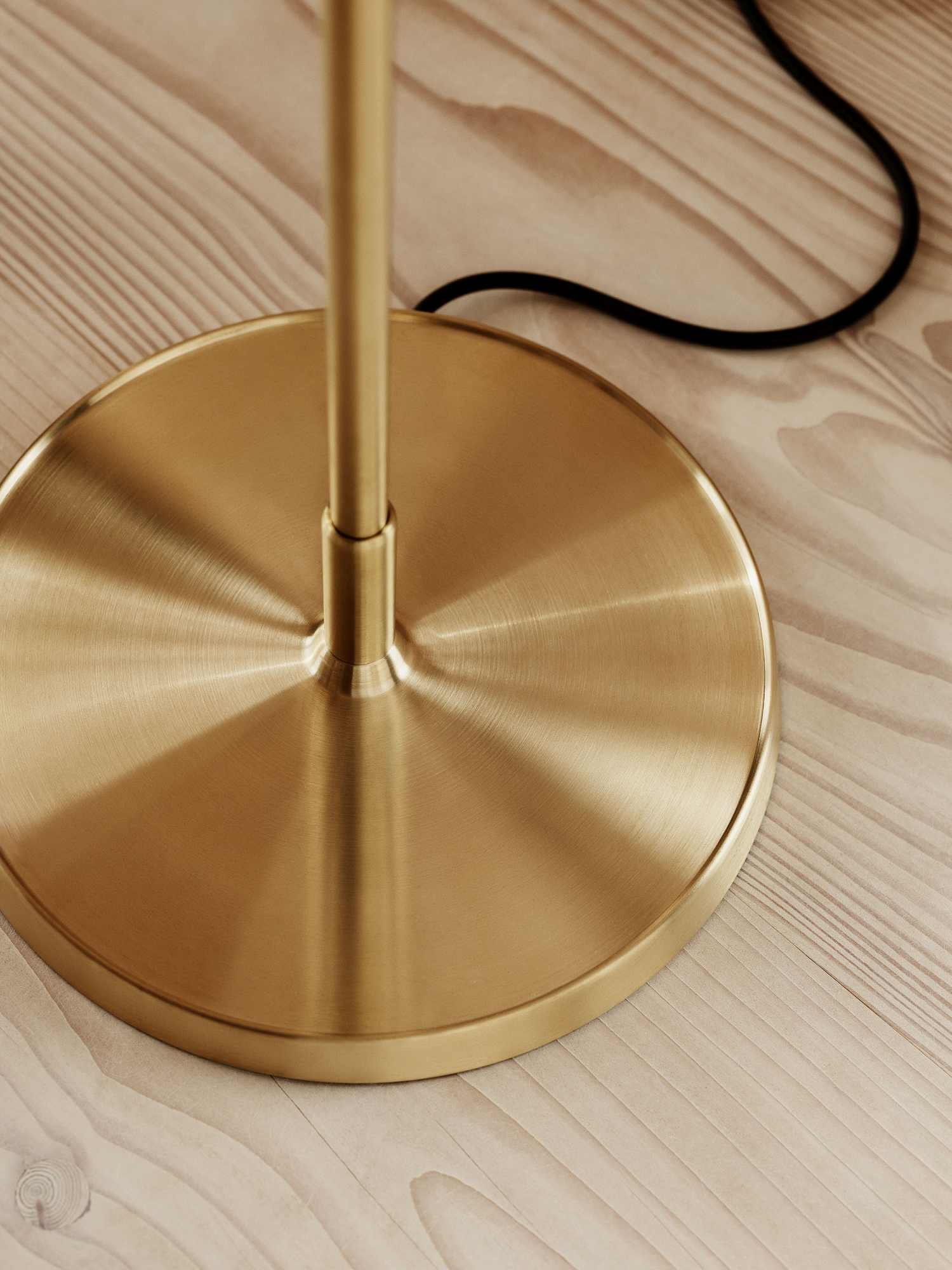 Detailaufnahme: Goldener Fuß der Clam Stehleuchte von Fritz Hansen auf hellem Holzboden.