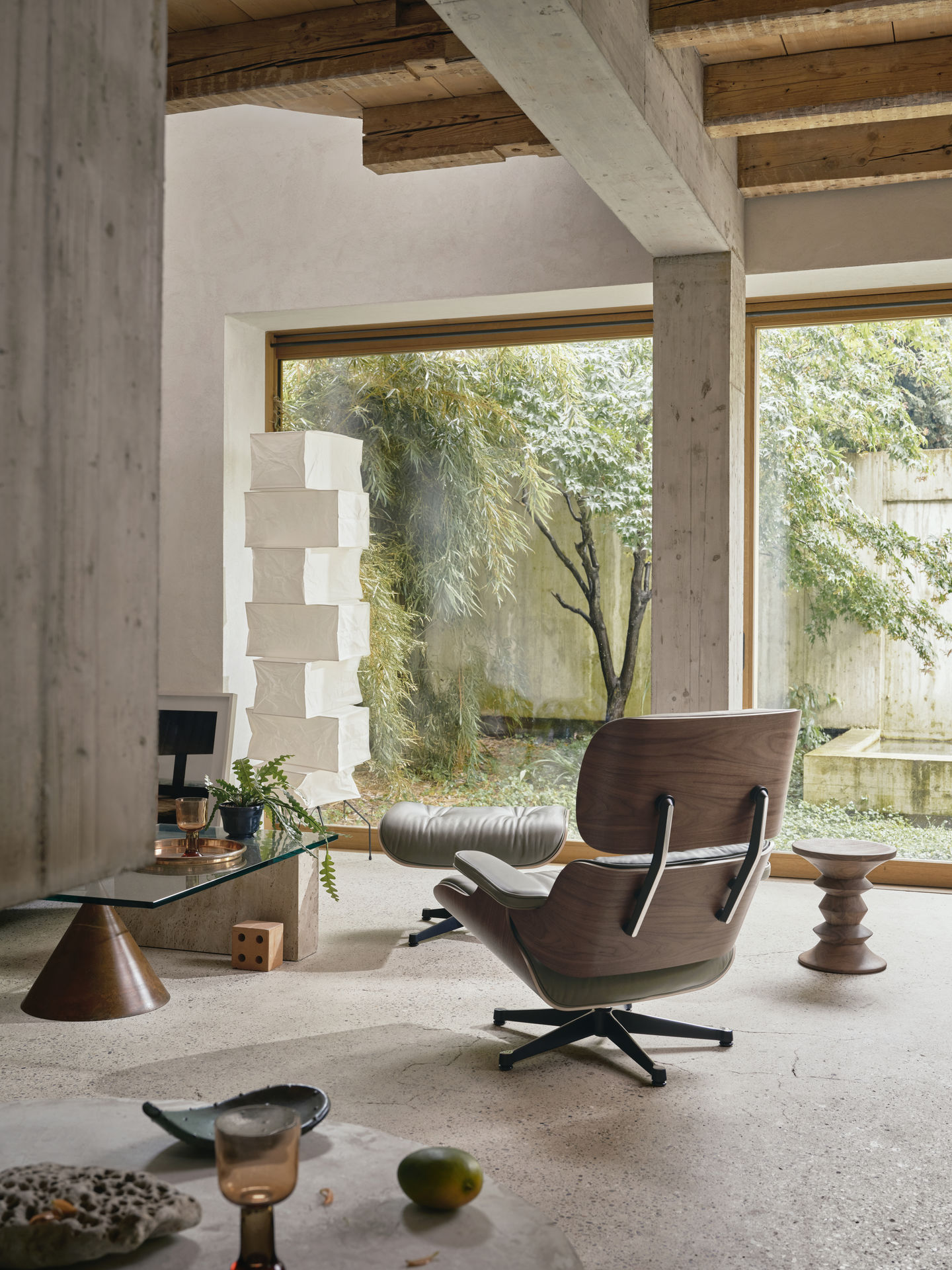 Eames Lounge Chair mit Ottoman in modernem Wohnraum mit Betonwänden und großem Fenster.