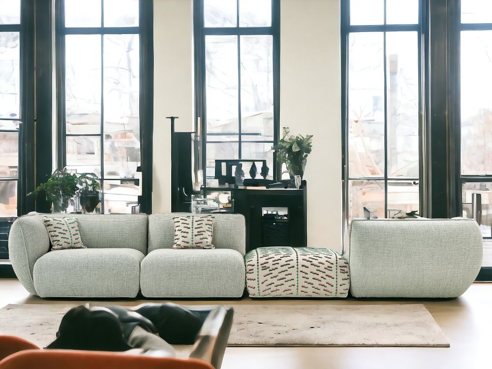 Mia Sofa von Freifrau: Modulares Sofa in hellgrauem Stoff mit passendem Hocker vor Fenster.