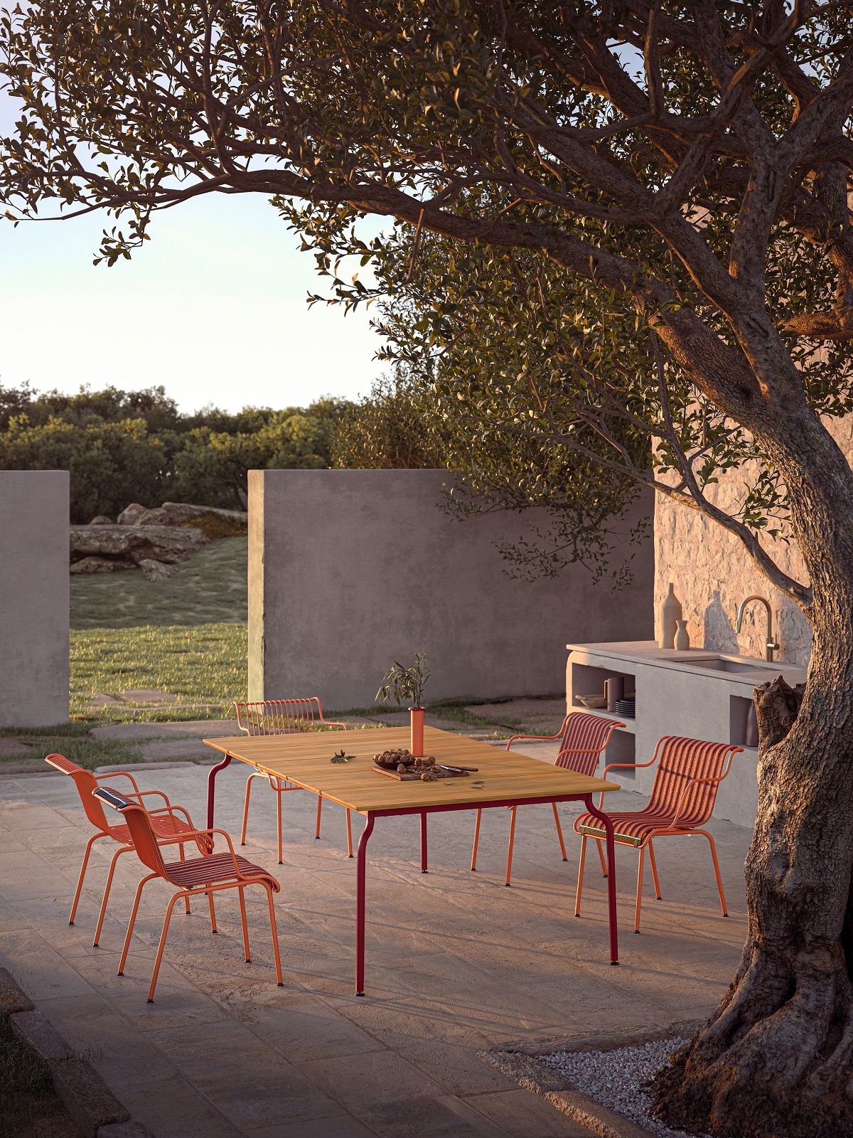 South Outdoor Chair Stuhl Magis: Gartenmöbel-Set mit Esstisch und orangefarbenen Stühlen unter Olivenbaum.