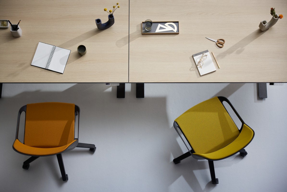 Zwei Numo Task Bürodrehstühle von Aeris in Gelb und Orange unter hellen Schreibtischen.