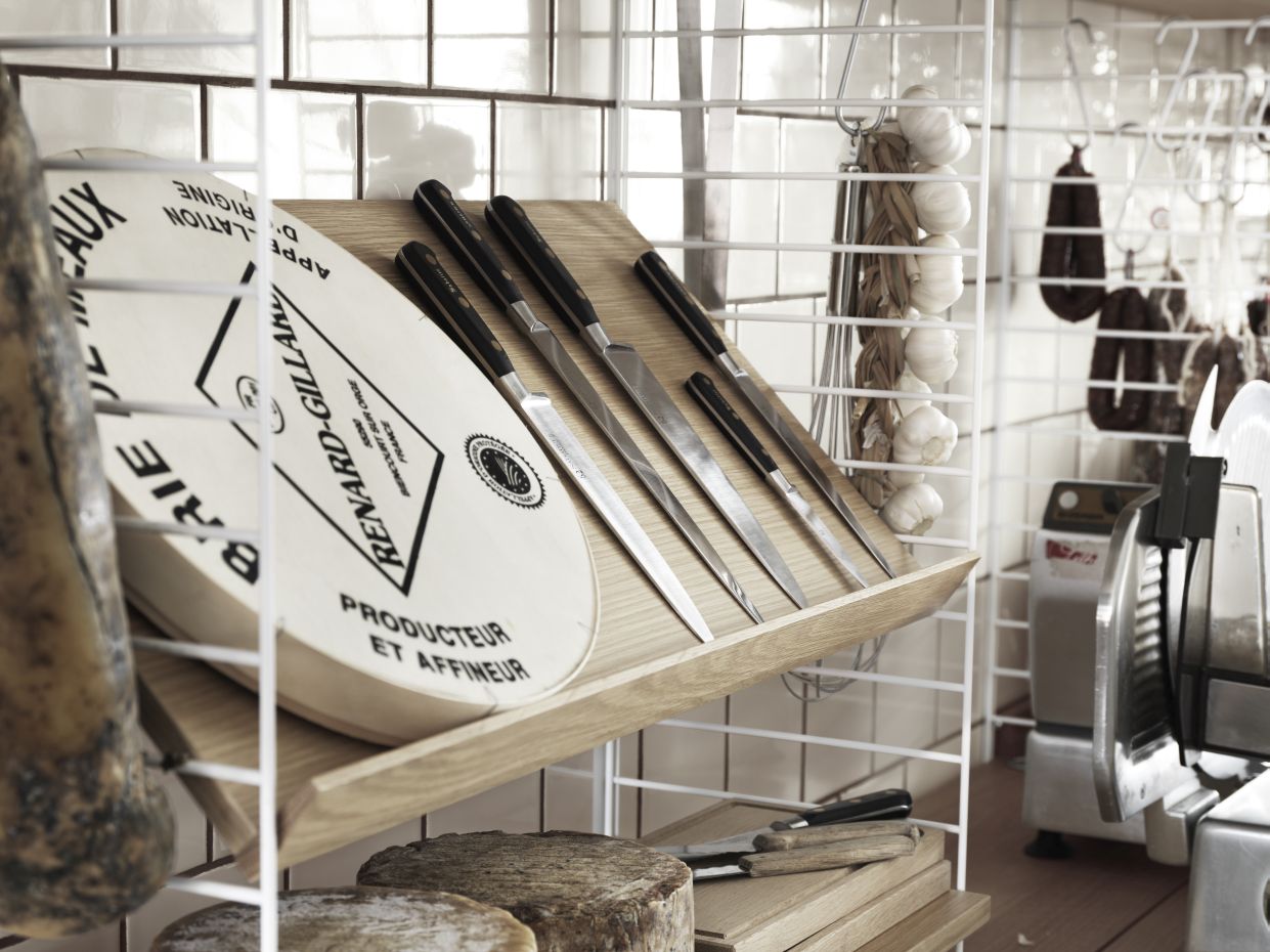 Eiche Zeitschriftenablage von String Furniture mit Käse, Messer und weiteren Lebensmitteln im Regal.