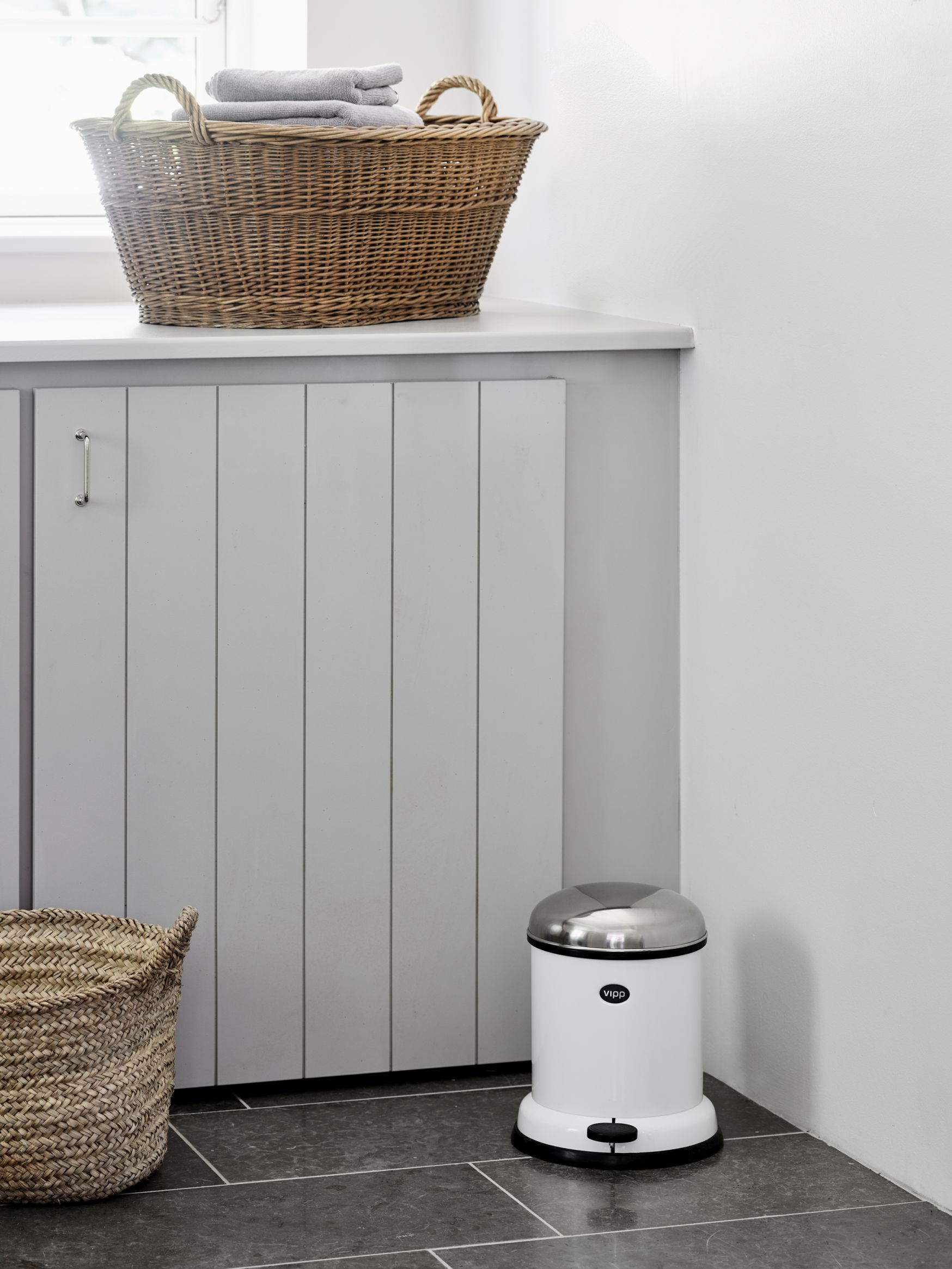 Weißer Vipp Treteimer aus Stahl mit Edelstahldeckel im Badezimmer, neben geflochtenen Körben.