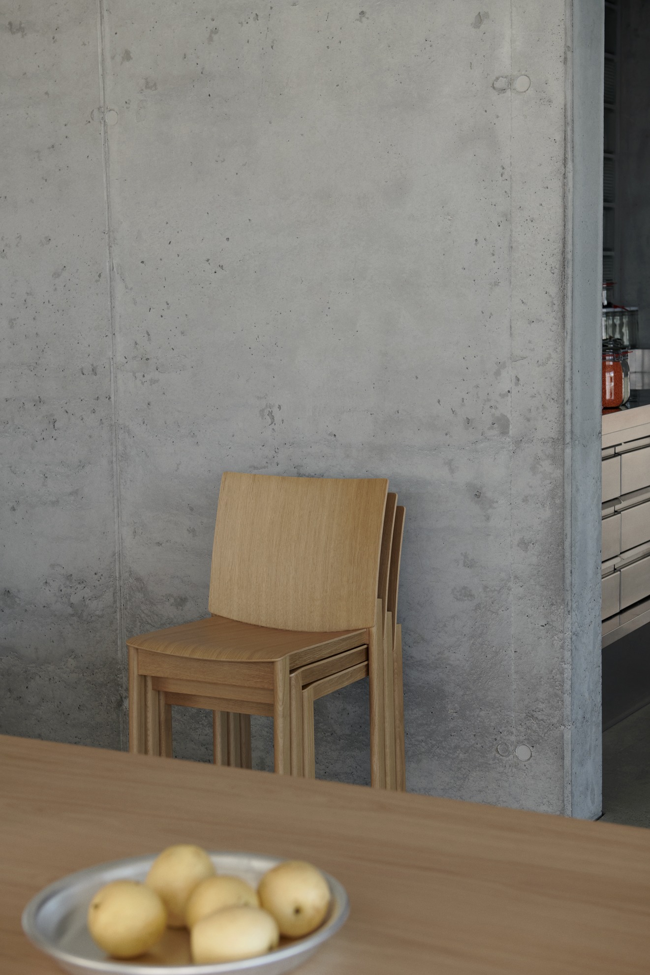 AndTradition Allwood AV35 Side Chair Stuhl aus hellem Holz, gestapelt vor einer Betonwand.