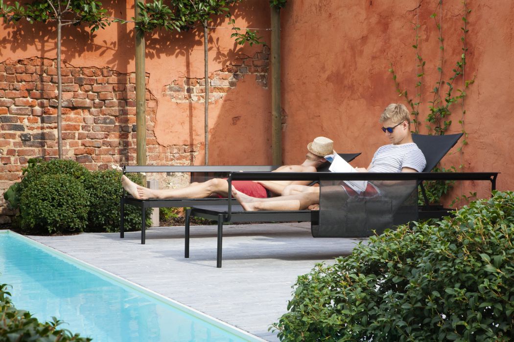 Zwei Männer entspannen auf der Sol + Luna Sonnenliege von Extremis im Außenbereich am Pool.