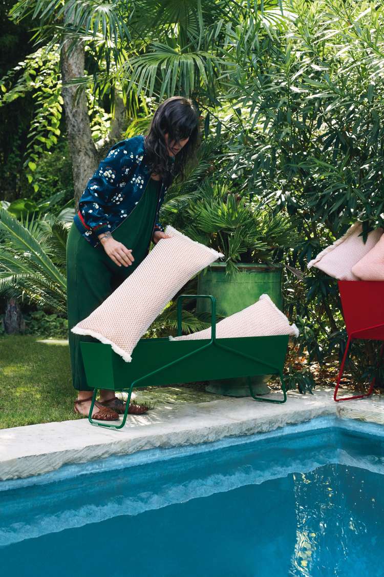 Frau platziert Kissen in grünen Fermob Basket Blumenkasten am Pool, Gartenmöbel und Dekoration.
