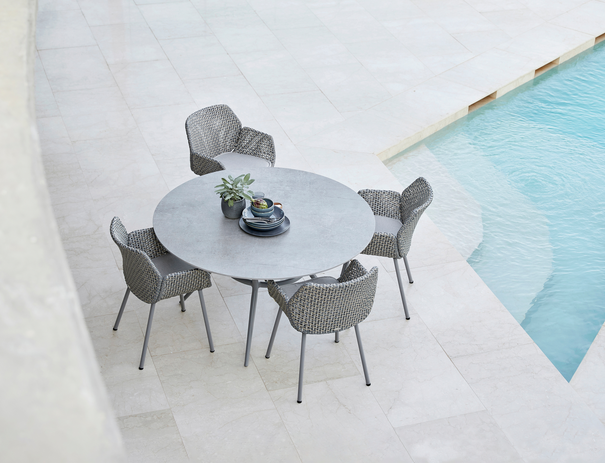 Cane-Line Vibe Sessel und runder Gartentisch aus grauem Geflecht am Pool für vier Personen.