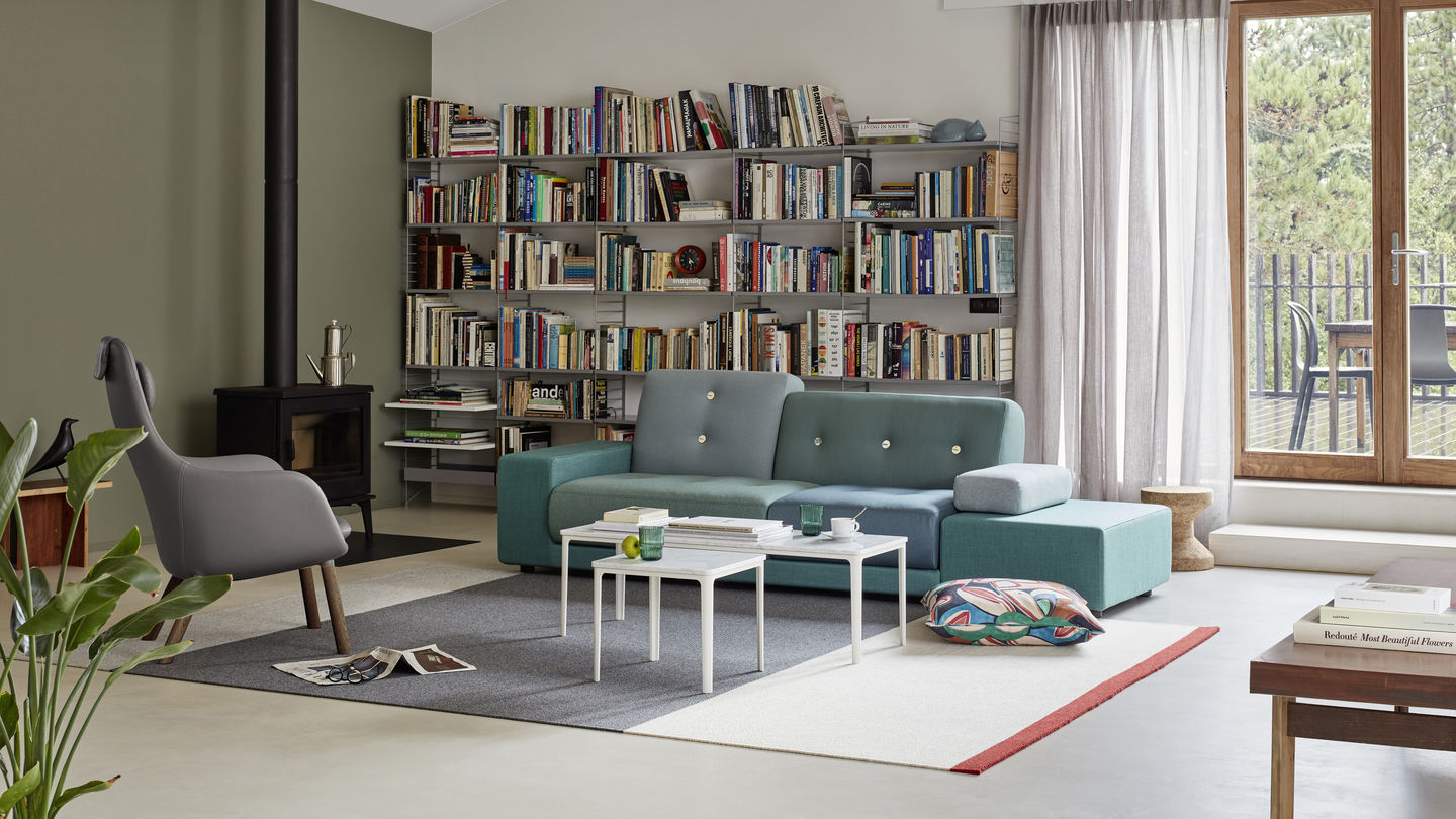 Wohnzimmer mit blau-grünem Polder Sofa von Vitra, Bücherregal, Kamin und Designermöbeln.