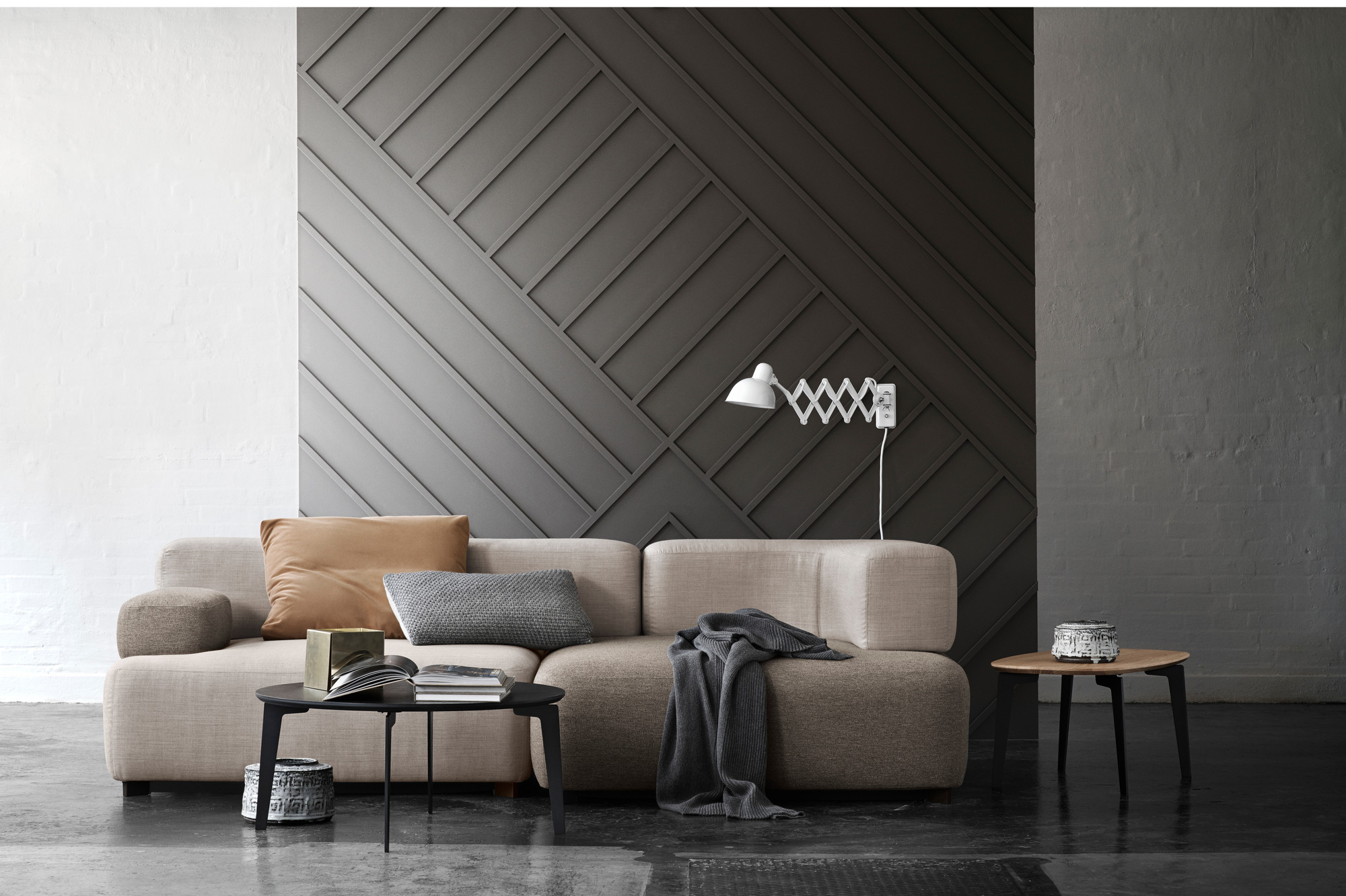 Weiße KAISER idell Scherenleuchte 6718 von Fritz Hansen an dunkler Wand über beigem Sofa.
