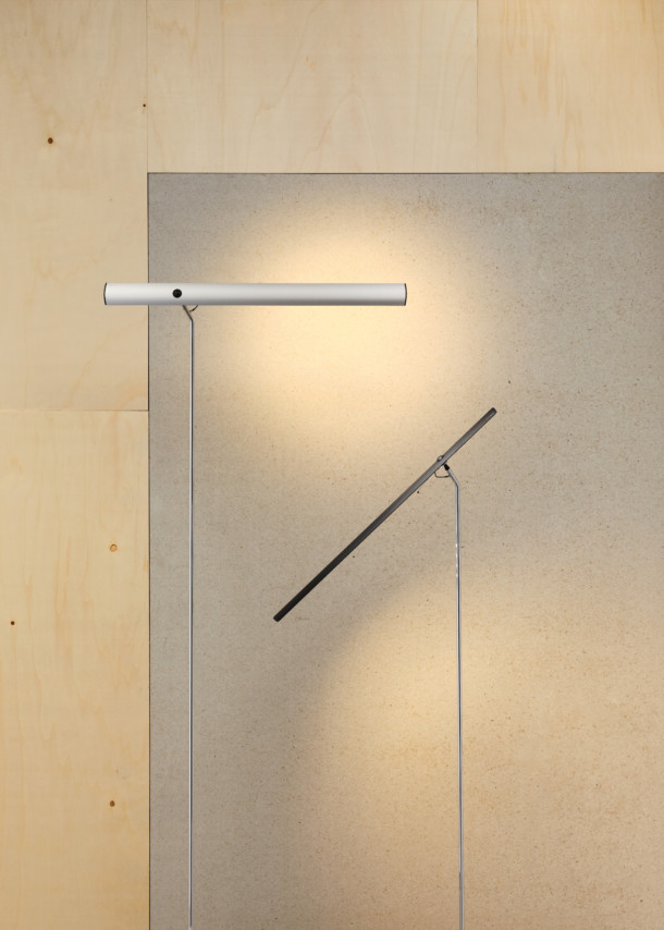 Zwei moderne LED-Stehleuchten in Silber und Schwarz vor einer Holz- und Betonwand.