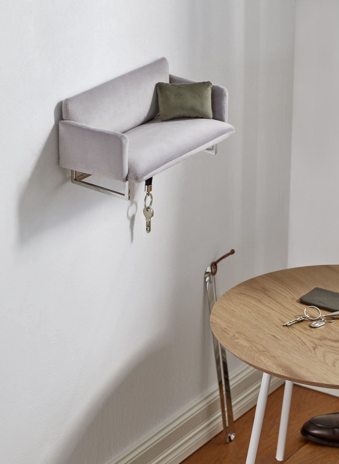 Graue Wandgarderobe in Sofaform mit Schlüsselanhänger und grünem Kissen, ideal für Flur und Eingangsbereich.