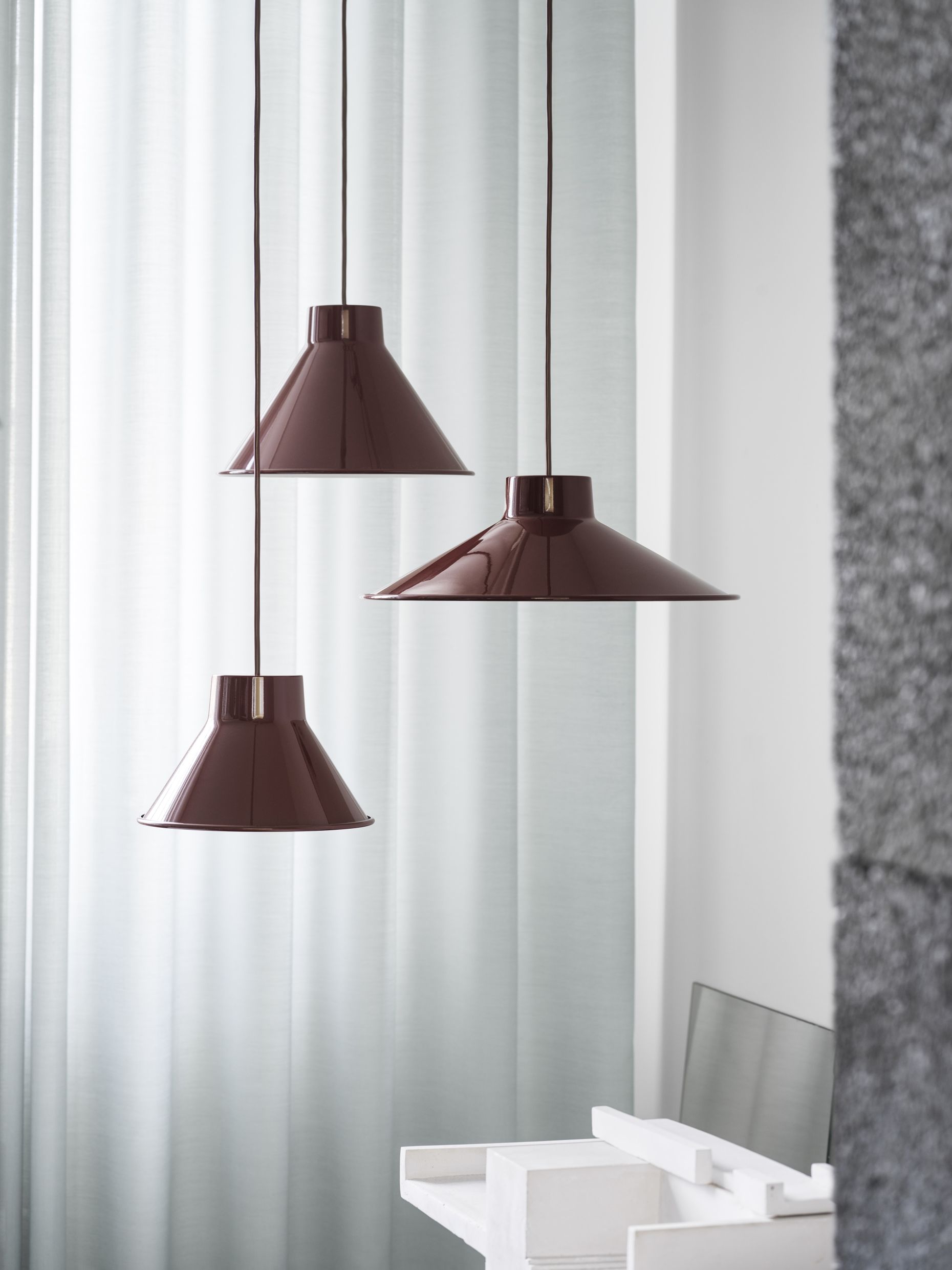 Drei Muuto Top Pendant Lamp Pendelleuchten in Grau hängen vor einem hellen Vorhang im Raum.