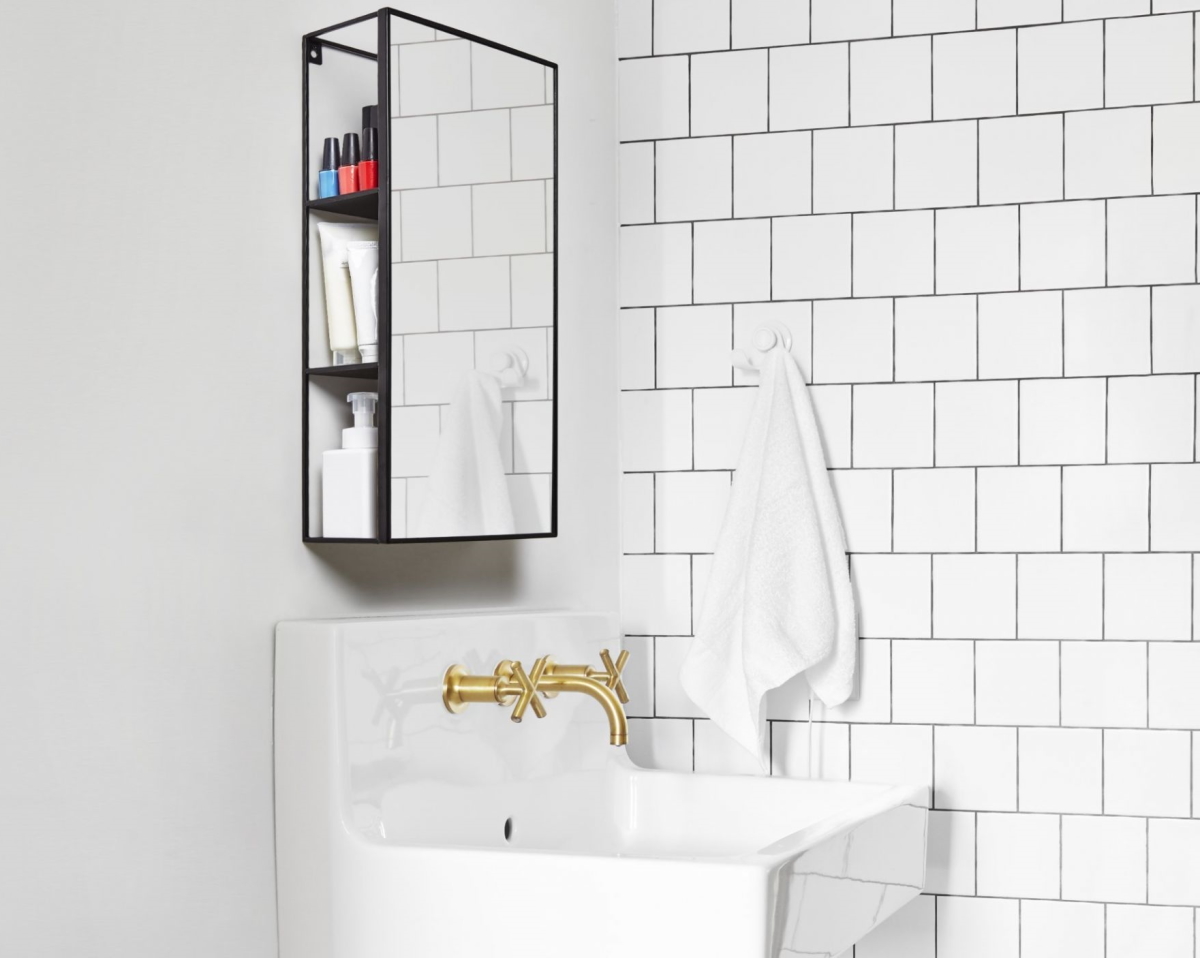 Modernes Badezimmer mit weißem Waschbecken, goldener Armatur und schwarzem Spiegelschrank mit Kosmetikprodukten.
