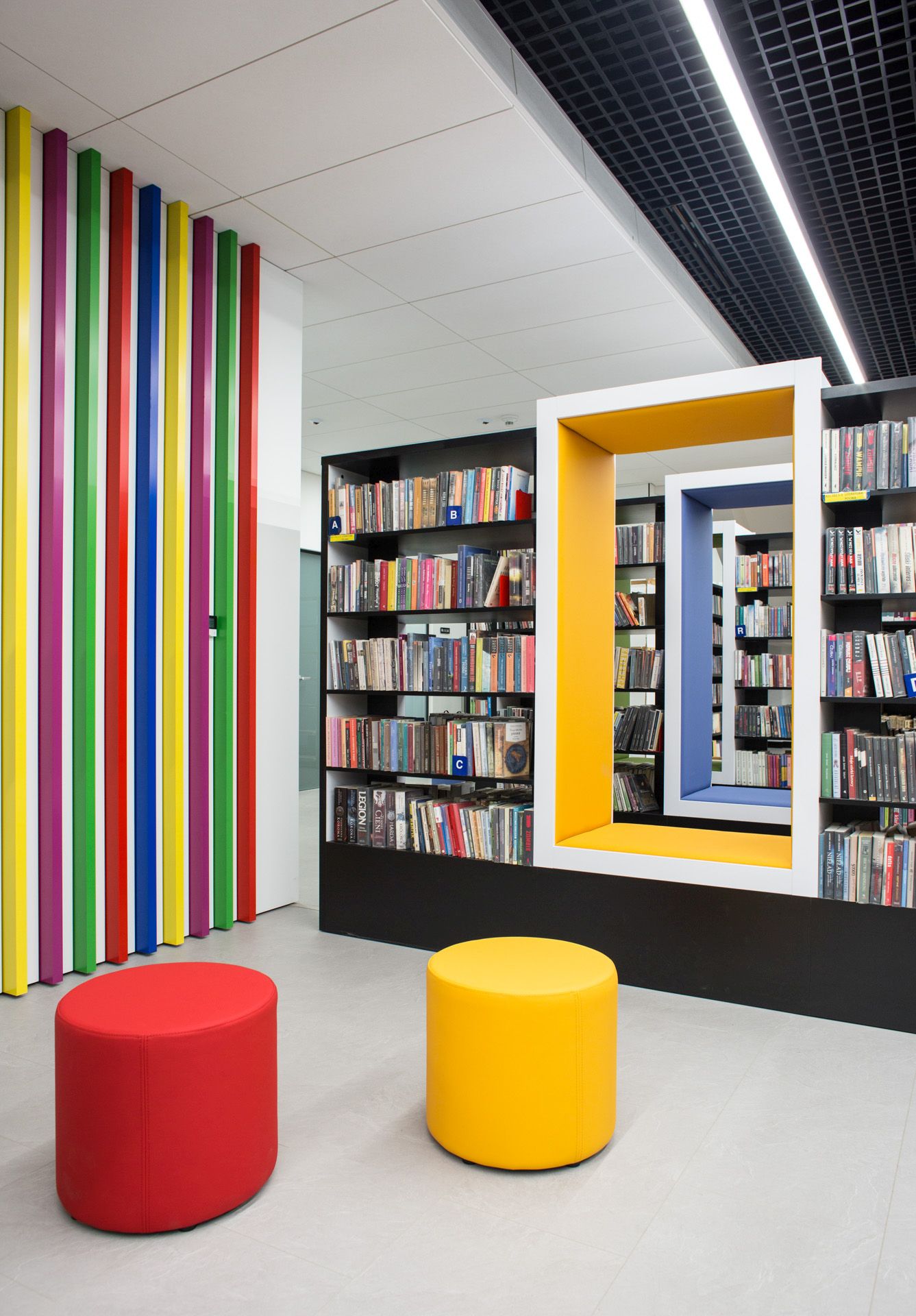Roter und gelber Bejot point POP R 450 Pouf Sitzhocker auf Rollen in moderner Bibliothek.