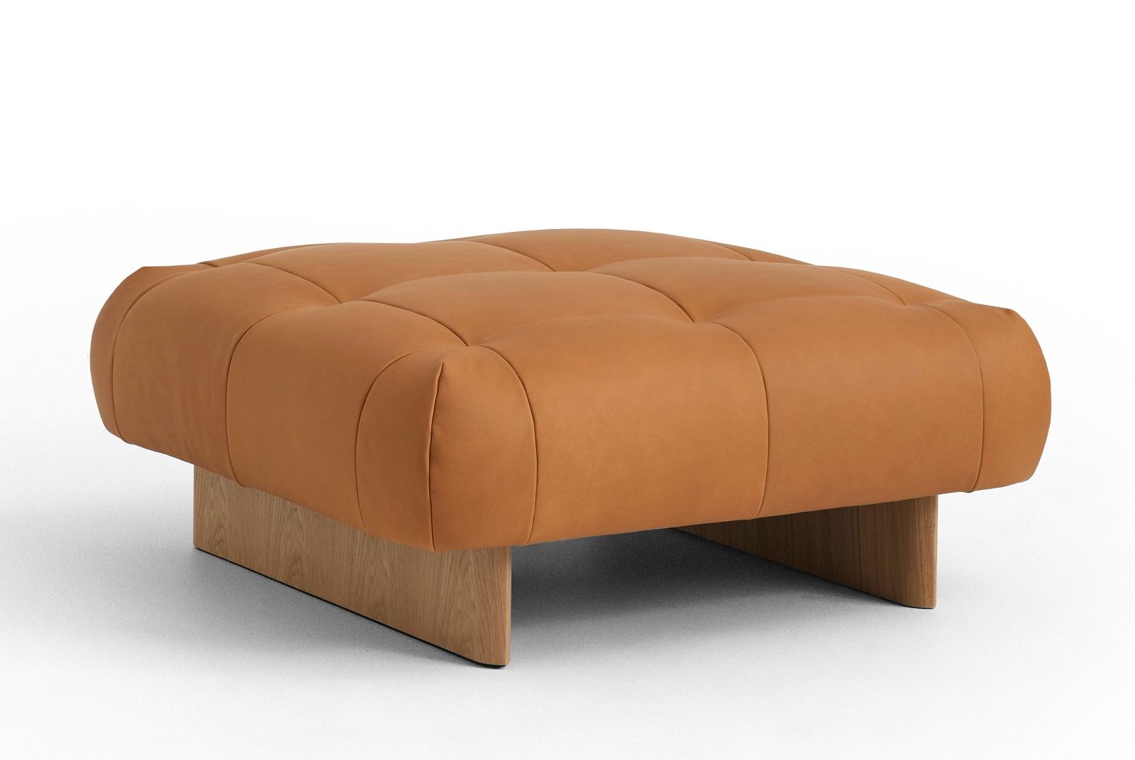 Quilton Ottoman Hocker von Hay, gepolstert mit braunem Leder auf einem hellen Holzsockel.