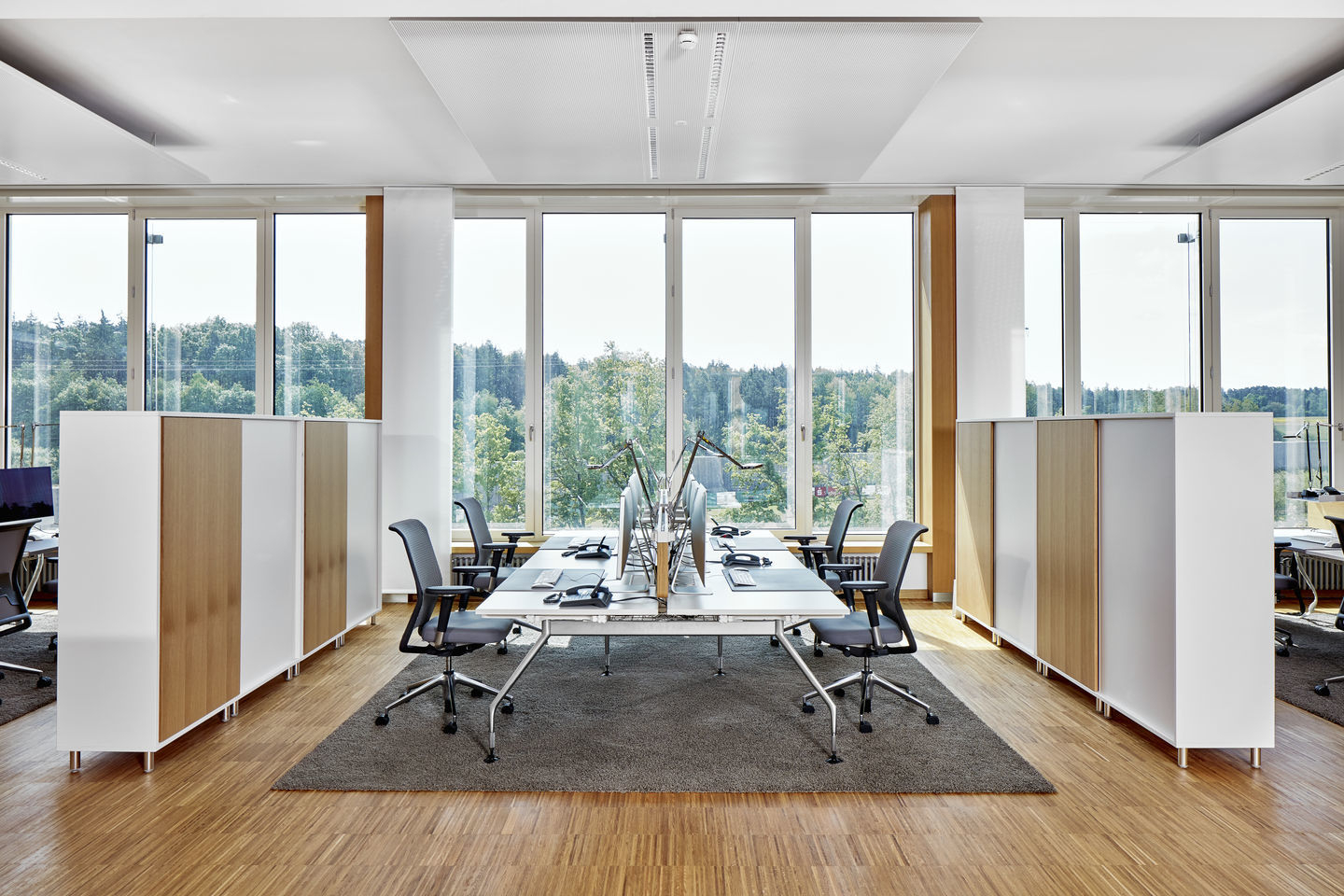 Heller Büroraum mit Vitra ID Mesh Bürodrehstühlen, weißen Schränken und großen Fenstern mit Blick ins Grüne.