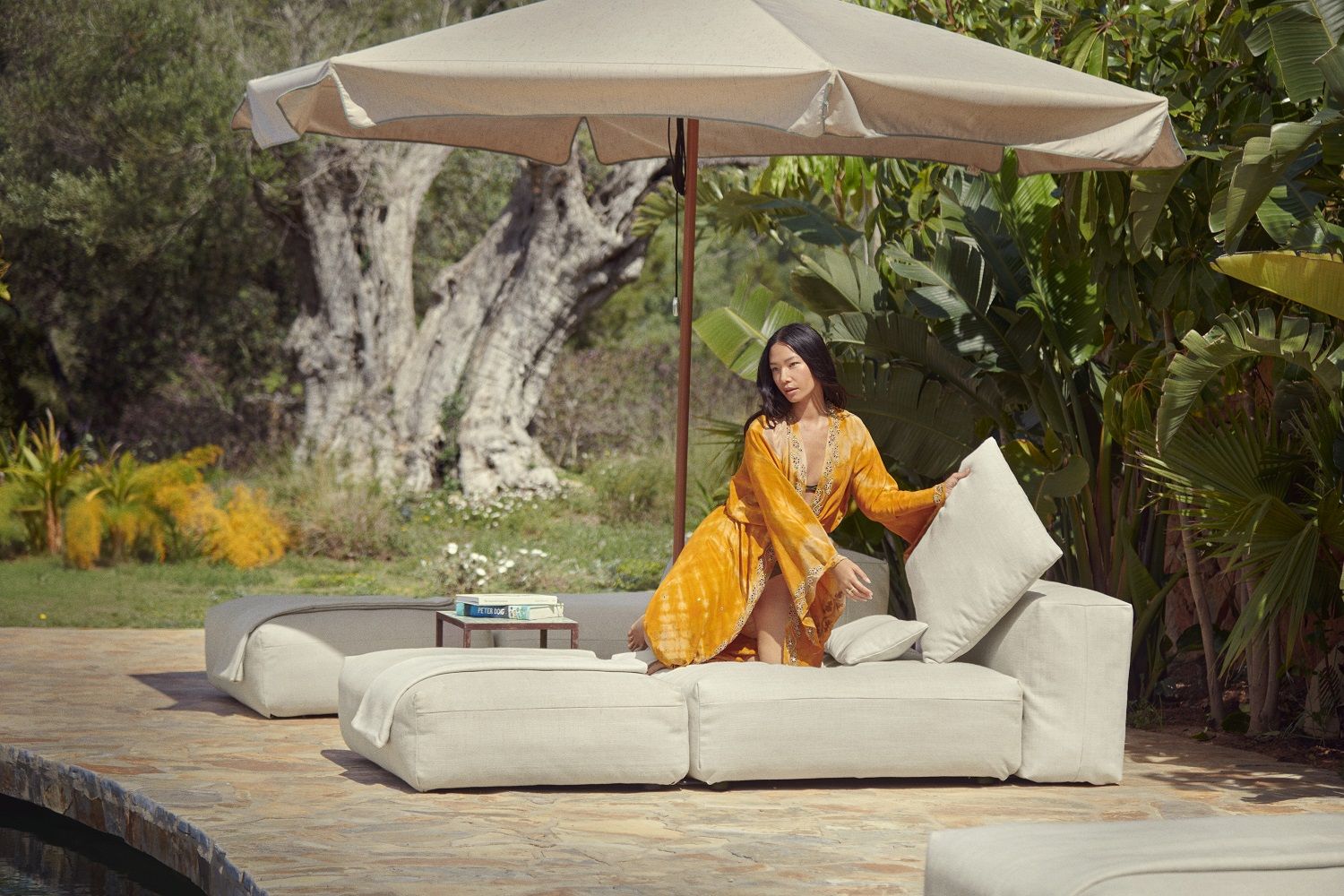 Frau entspannt auf modularem vetsak Outdoor Sofa mit Noodle Pillow Pique Kissen unter Sonnenschirm.