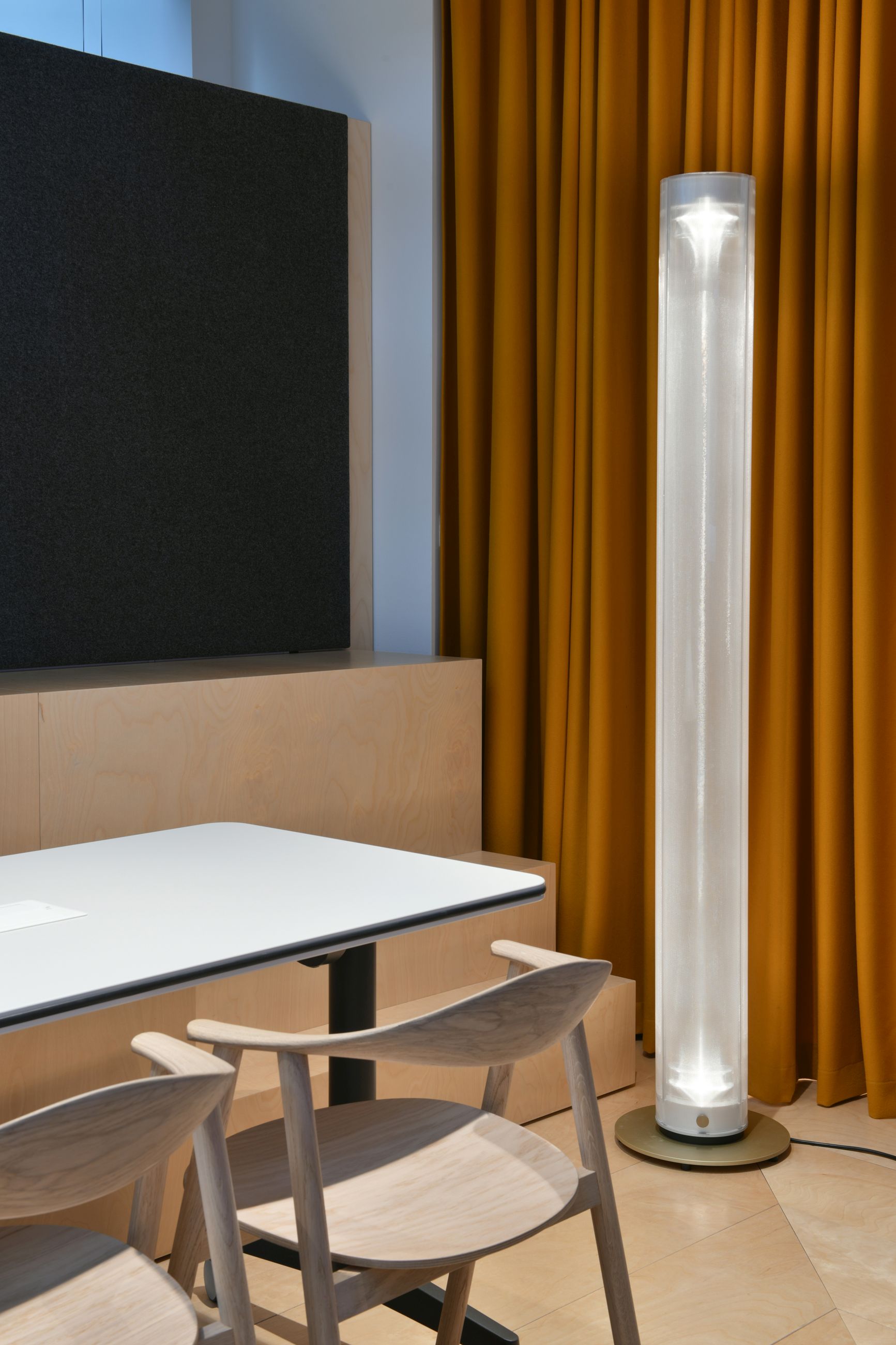 Twilight Stehleuchte von Belux, eine moderne, zylindrische Lampe mit warmem Licht, im Büro neben Tisch und Vorhang.