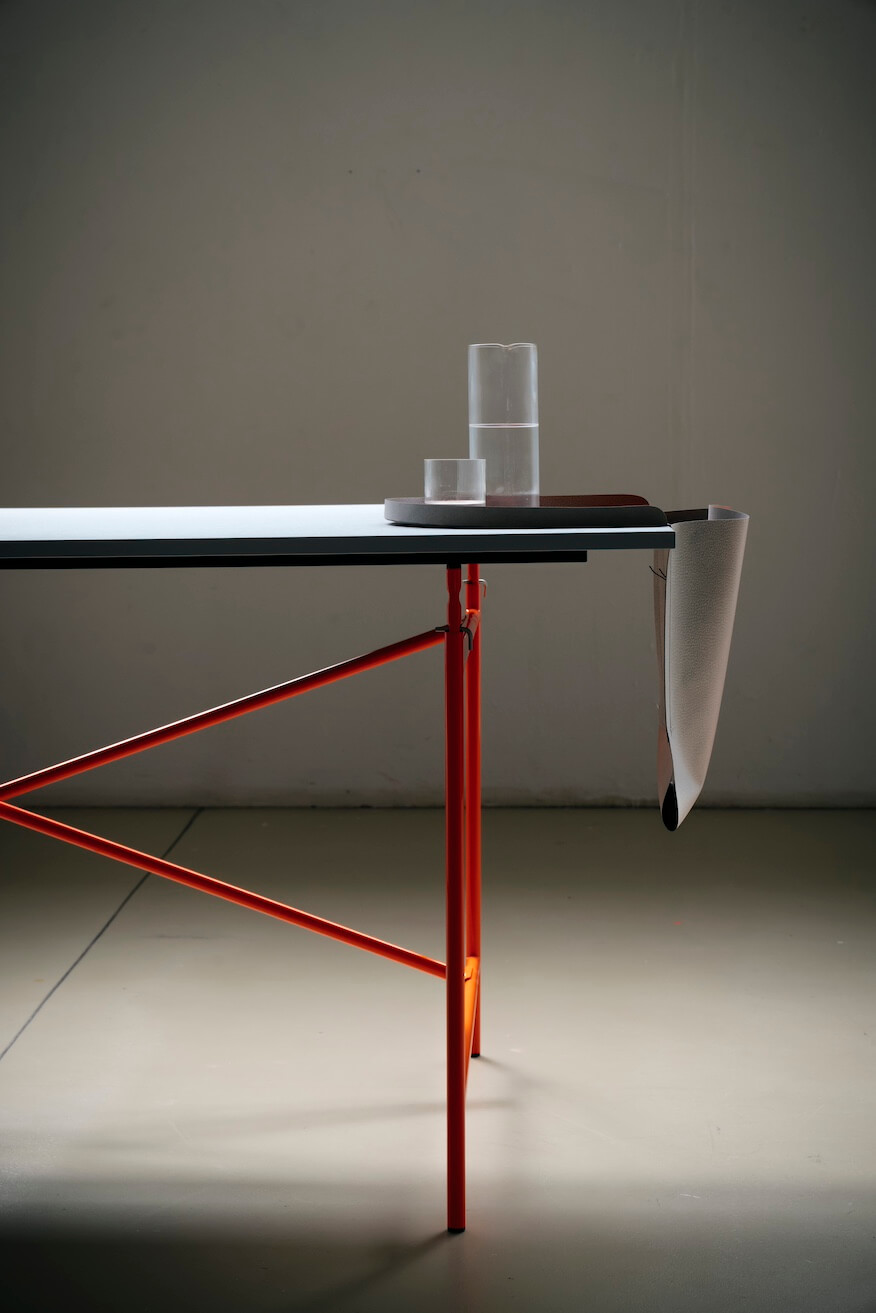 Moderner Schreibtisch mit rotem Metallgestell und Glas auf einem Tablett, minimalistisches Design für Büro oder Zuhause.