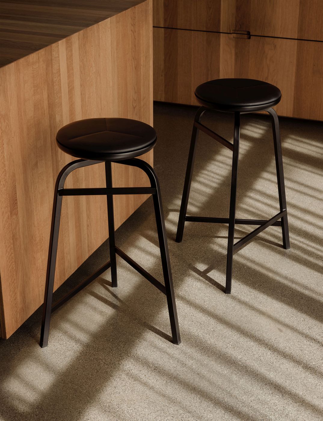 Zwei Treble Barhocker von Northern mit schwarzem Ledersitz und dunklem Metallgestell vor Holzküchenzeile.