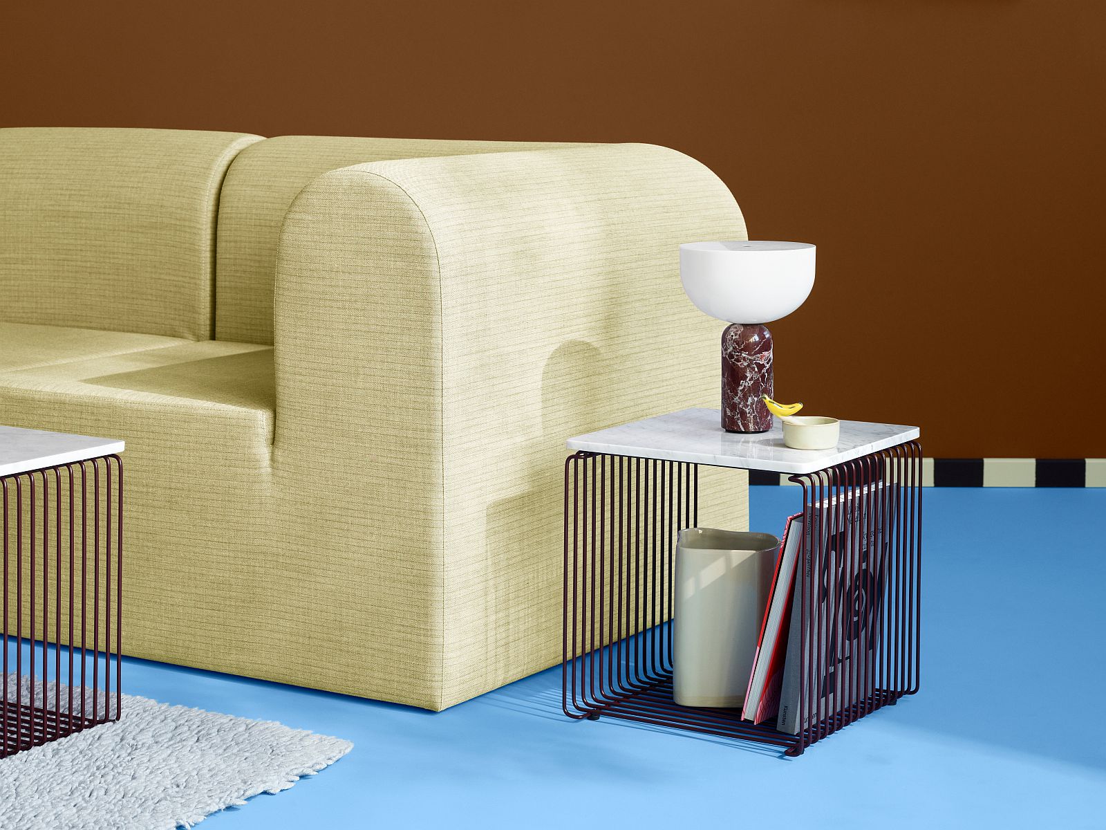 Nahaufnahme eines Panton Wire Regals mit Marmor Abdeckplatte, Lampe und Dekoration neben einem beigen Sofa.