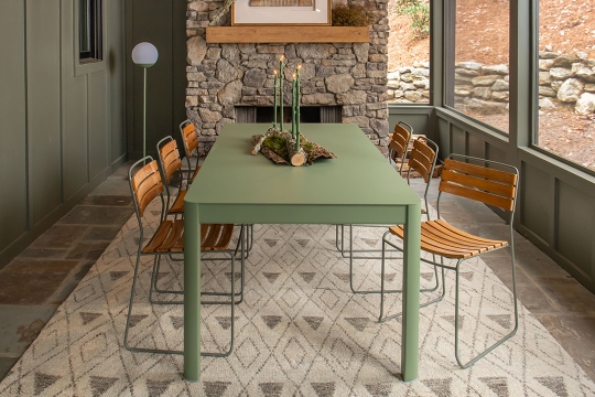 Fermob Surprising Teak Chair Outdoor: Detailaufnahme von Holzstühlen und einem grünen Tisch auf einem gemusterten Teppich.
