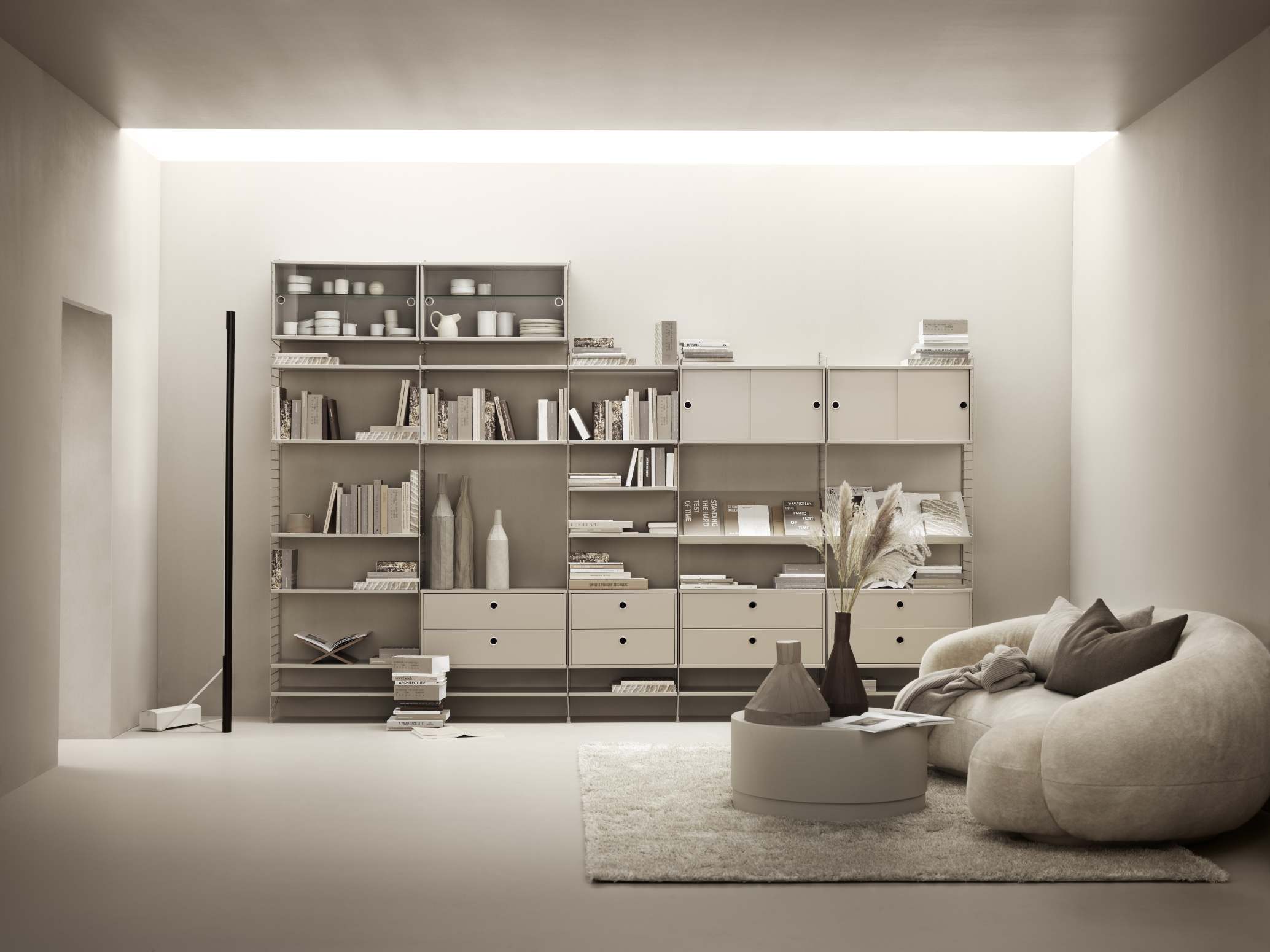 Helles Wohnzimmer mit String Furniture Regalsystem, bequemen Sessel, Teppich und minimalistischer Dekoration für modernes Wohnen.