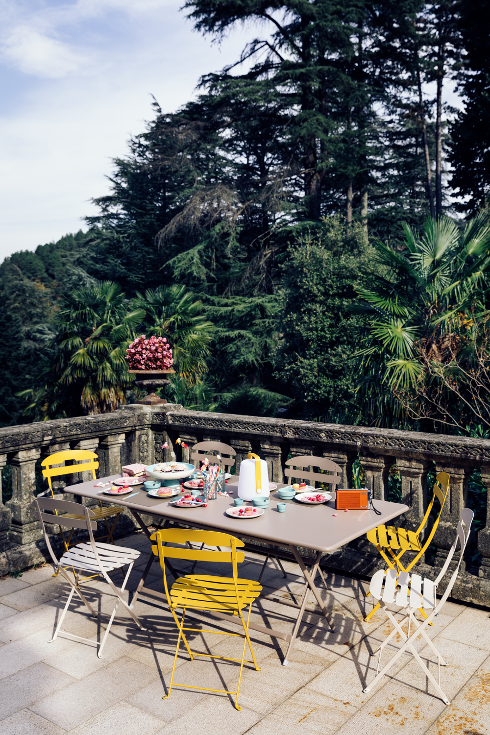 Caractere Fermob Klapptisch eckig mit Stühlen auf einer Terrasse, gedeckt mit Geschirr für eine Gartenparty.